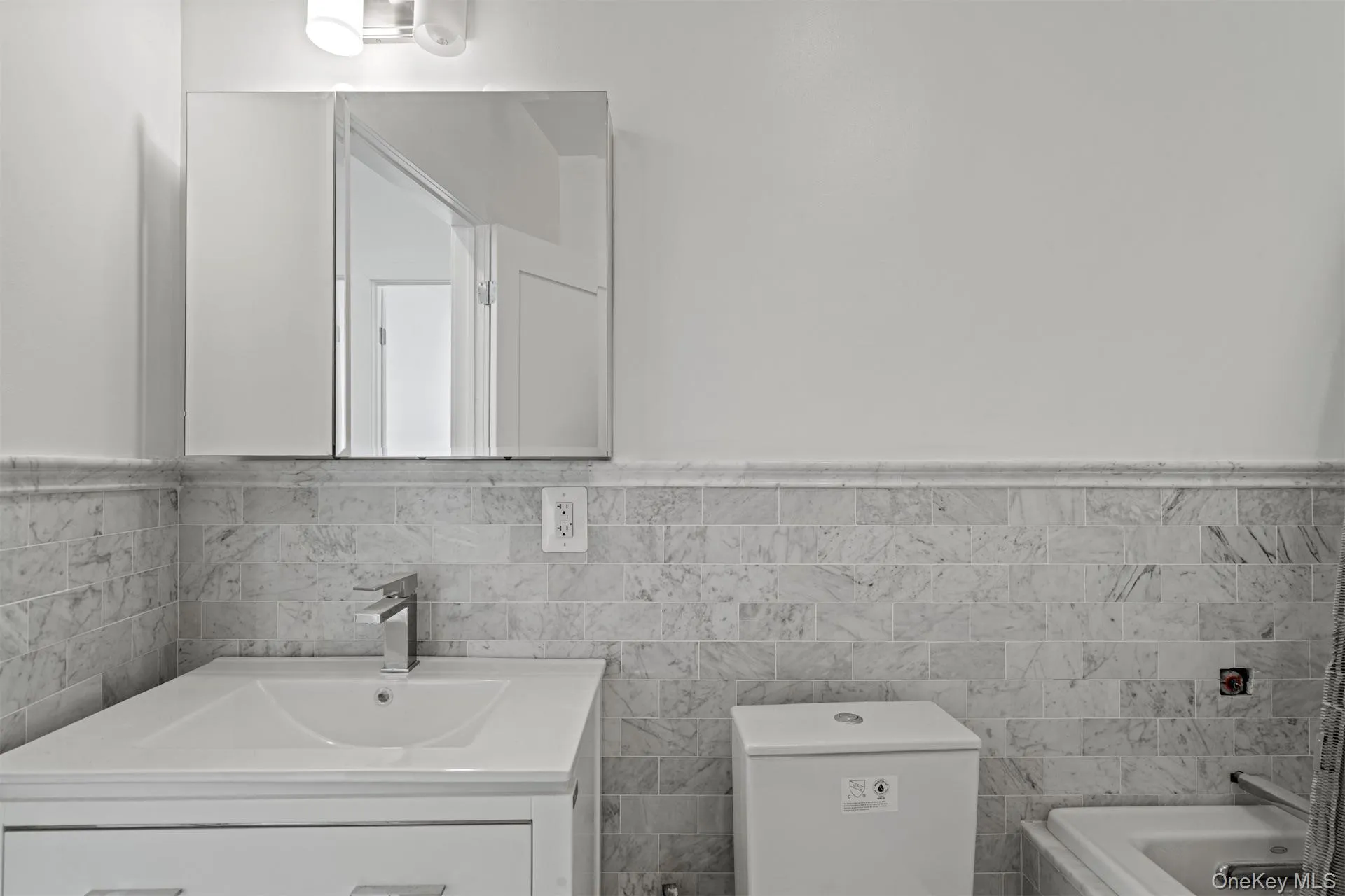 Full bathroom featuring a tub to relax in, vanity, a wainscoted wall, and tile walls Full bathroom featuring a tub to relax in, vanity, a wainscoted wall, and tile walls