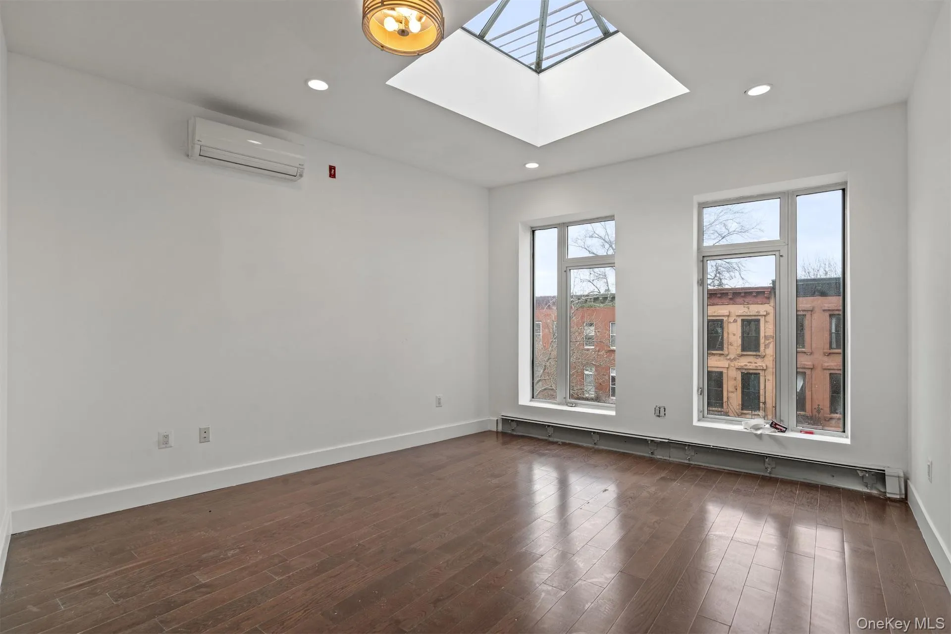 Unfurnished room featuring a skylight, dark wood-type flooring, a wall mounted AC, baseboard heating, and recessed lighting Unfurnished room featuring a skylight, dark wood-type flooring, a wall mounted AC, baseboard heating, and recessed lighting