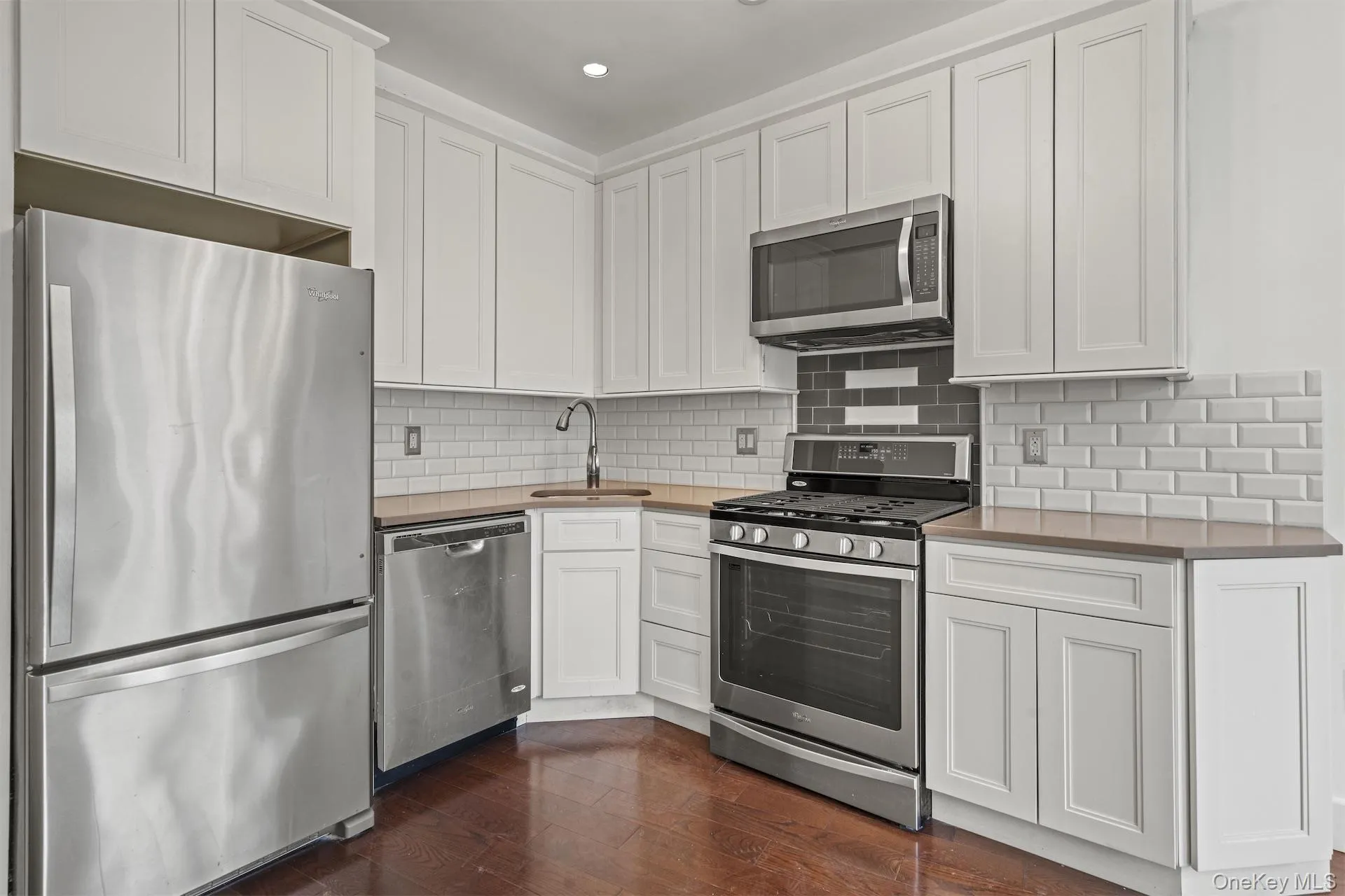 Kitchen with appliances with stainless steel finishes, white cabinets, dark wood-style floors, decorative backsplash, and recessed lighting Kitchen with appliances with stainless steel finishes, white cabinets, dark wood-style floors, decorative backsplash, and recessed lighting