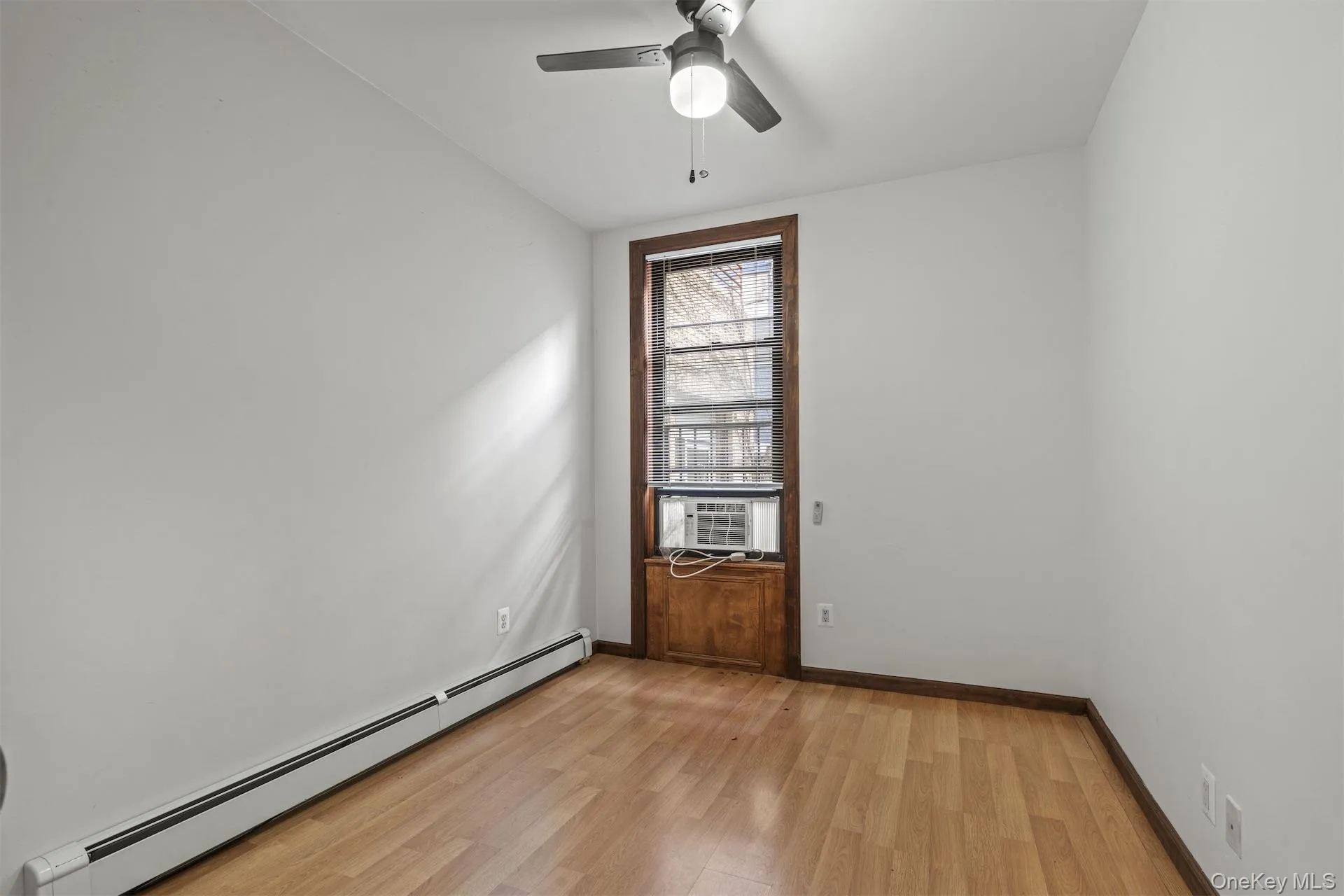 Spare room featuring a baseboard heating unit, light wood-style floors, ceiling fan, and cooling unit Spare room featuring a baseboard heating unit, light wood-style floors, ceiling fan, and cooling unit