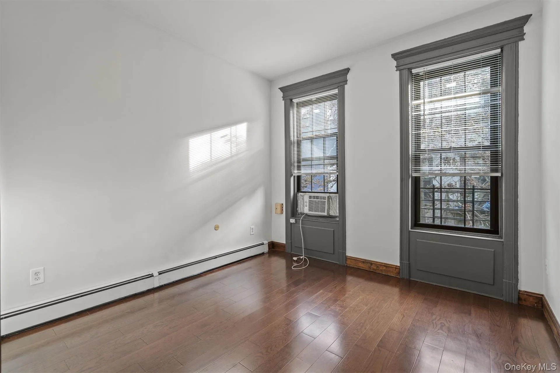 Unfurnished room with baseboard heating, dark wood-style flooring, and cooling unit Unfurnished room with baseboard heating, dark wood-style flooring, and cooling unit