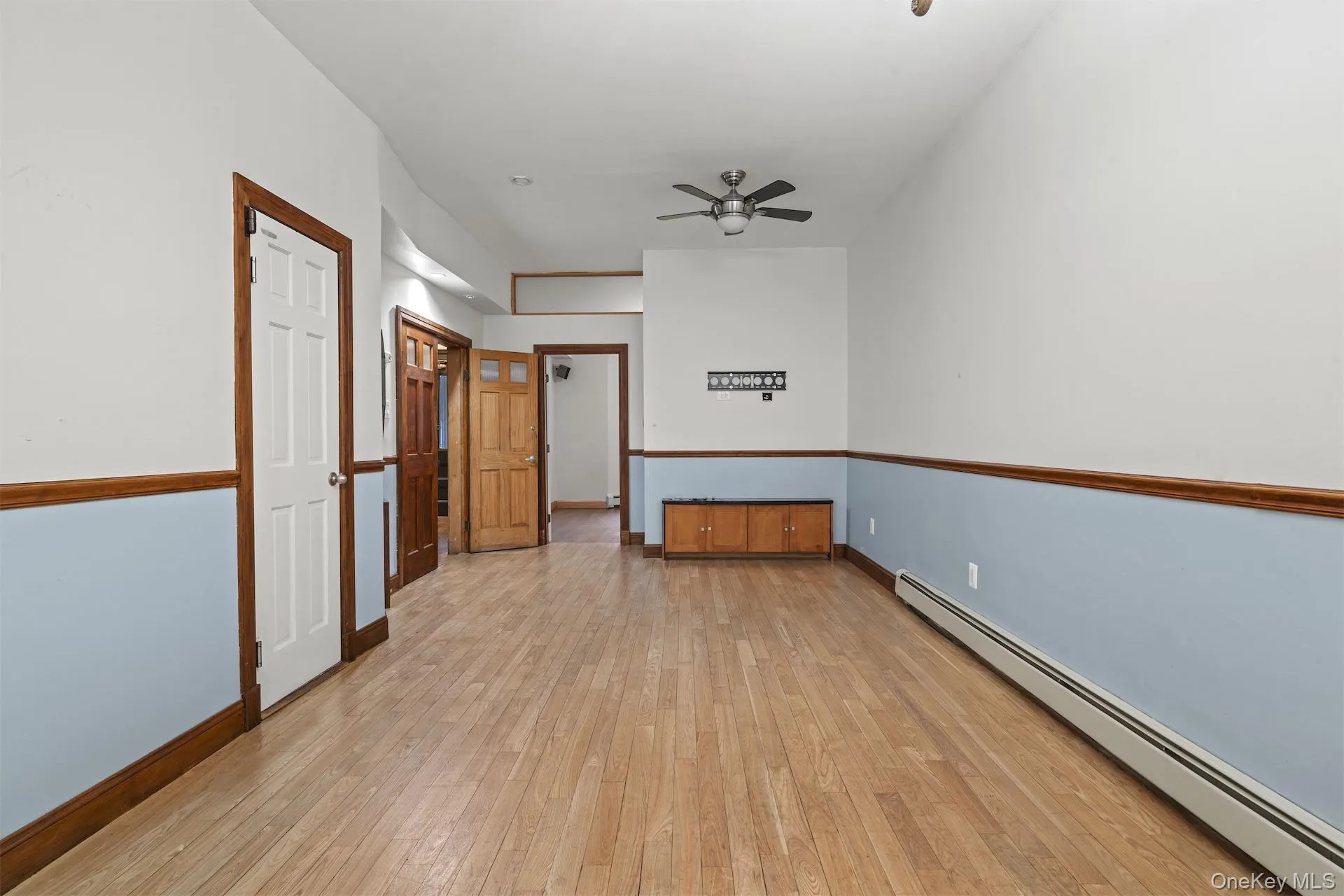 Empty room featuring a baseboard radiator, light wood finished floors, and a ceiling fan Empty room featuring a baseboard radiator, light wood finished floors, and a ceiling fan