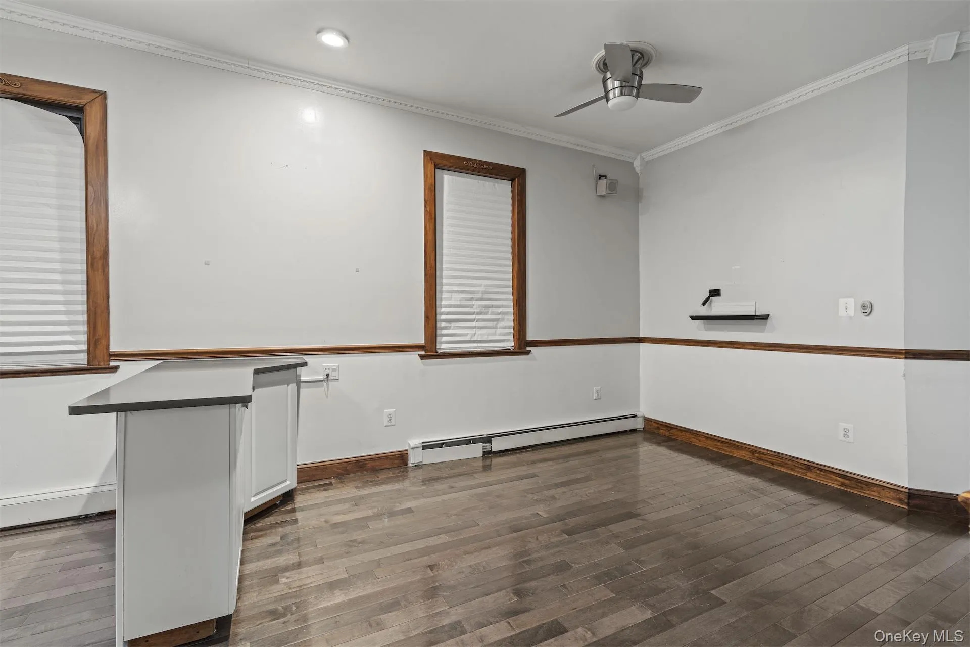 Spare room featuring ornamental molding, baseboard heating, dark wood-style floors, and ceiling fan Spare room featuring ornamental molding, baseboard heating, dark wood-style floors, and ceiling fan