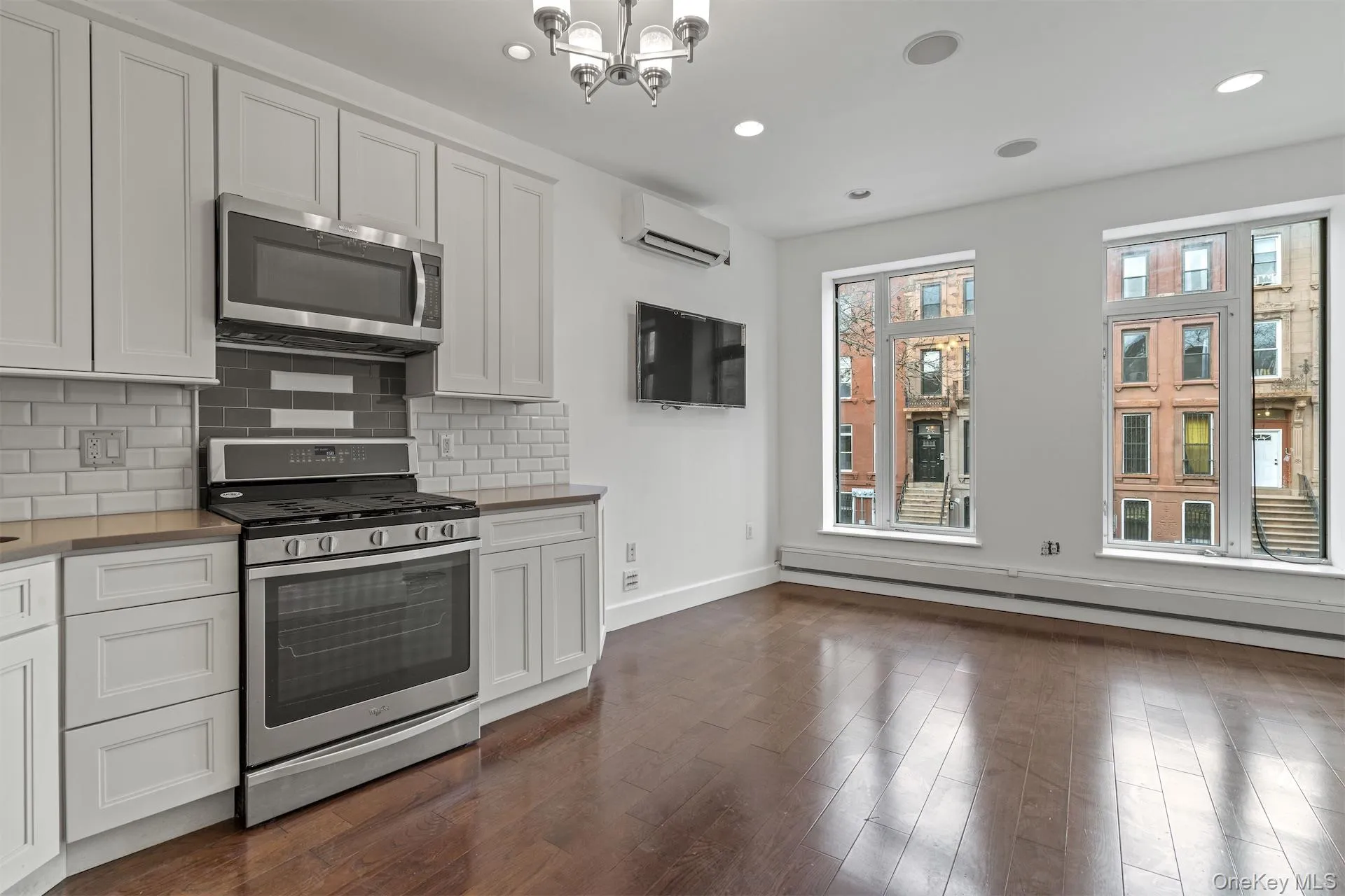 Kitchen featuring stainless steel appliances, decorative backsplash, white cabinetry, dark wood-type flooring, and baseboard heating Kitchen featuring stainless steel appliances, decorative backsplash, white cabinetry, dark wood-type flooring, and baseboard heating
