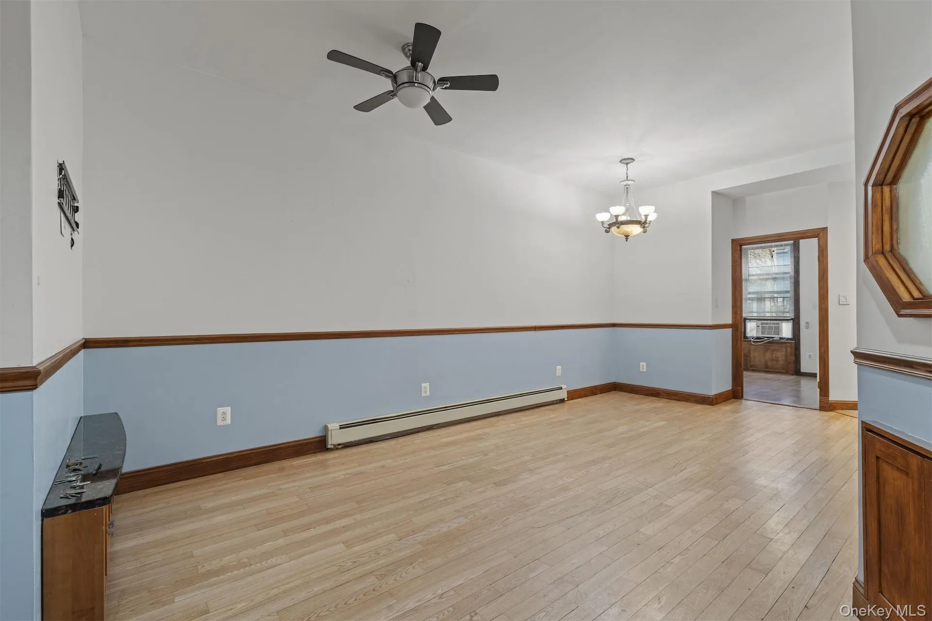 Empty room with light wood-type flooring, baseboard heating, a chandelier, and ceiling fan Empty room with light wood-type flooring, baseboard heating, a chandelier, and ceiling fan