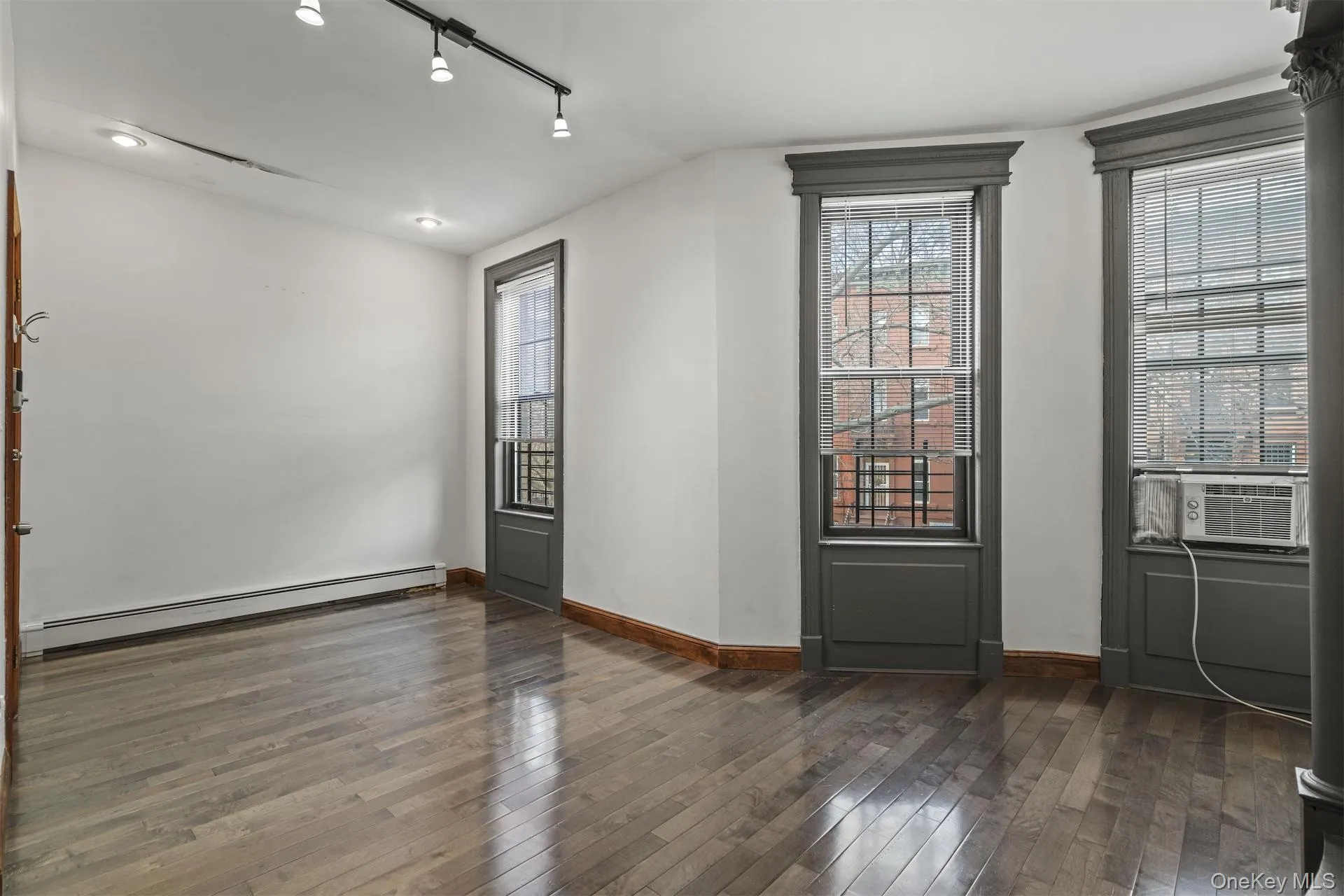 Empty room featuring baseboard heating, rail lighting, dark wood finished floors, and cooling unit Empty room featuring baseboard heating, rail lighting, dark wood finished floors, and cooling unit