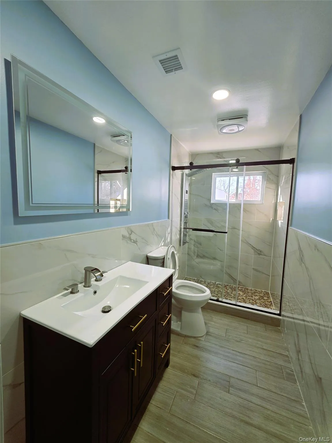 Bathroom featuring a dark wood-finish vanity with gold-tone hardware, a rectangular undermount sink, and a framed wall mirror Bathroom featuring a dark wood-finish vanity with gold-tone hardware, a rectangular undermount sink, and a framed wall mirror