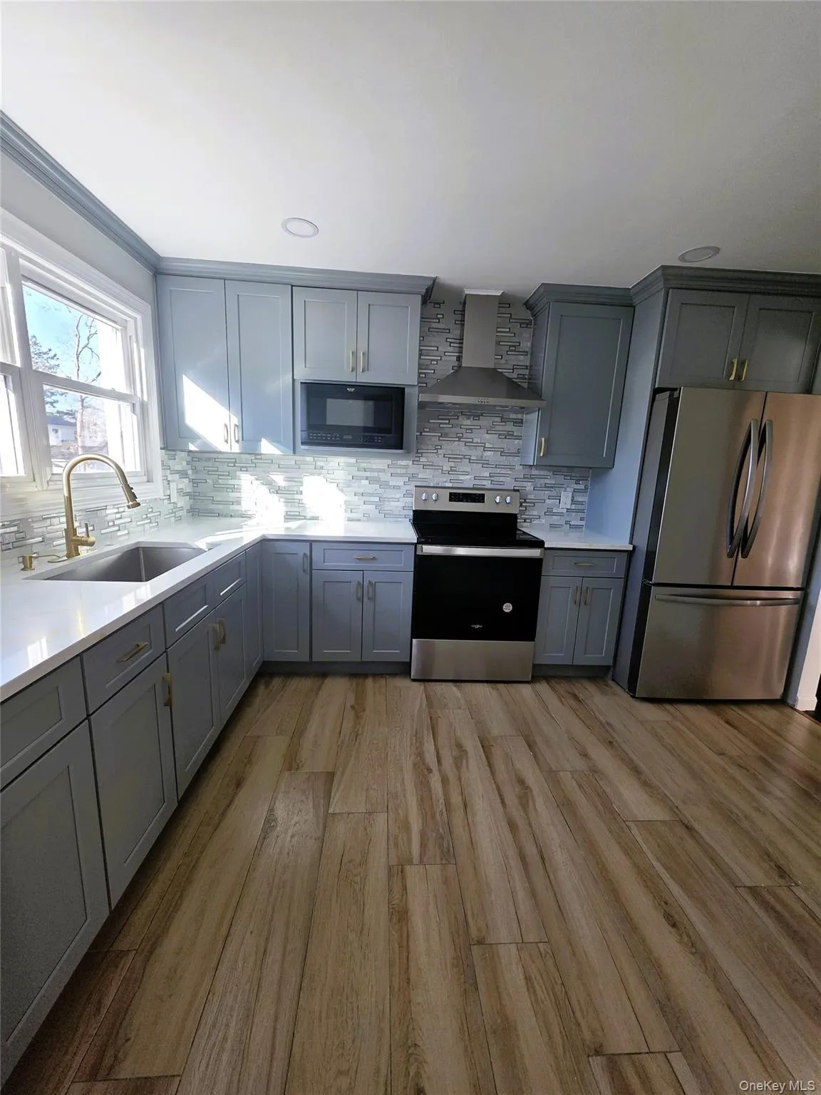 Kitchen featuring light blue cabinetry, stainless steel appliances, wood-finish flooring, white countertops, and a textured tile backsplash Kitchen featuring light blue cabinetry, stainless steel appliances, wood-finish flooring, white countertops, and a textured tile backsplash