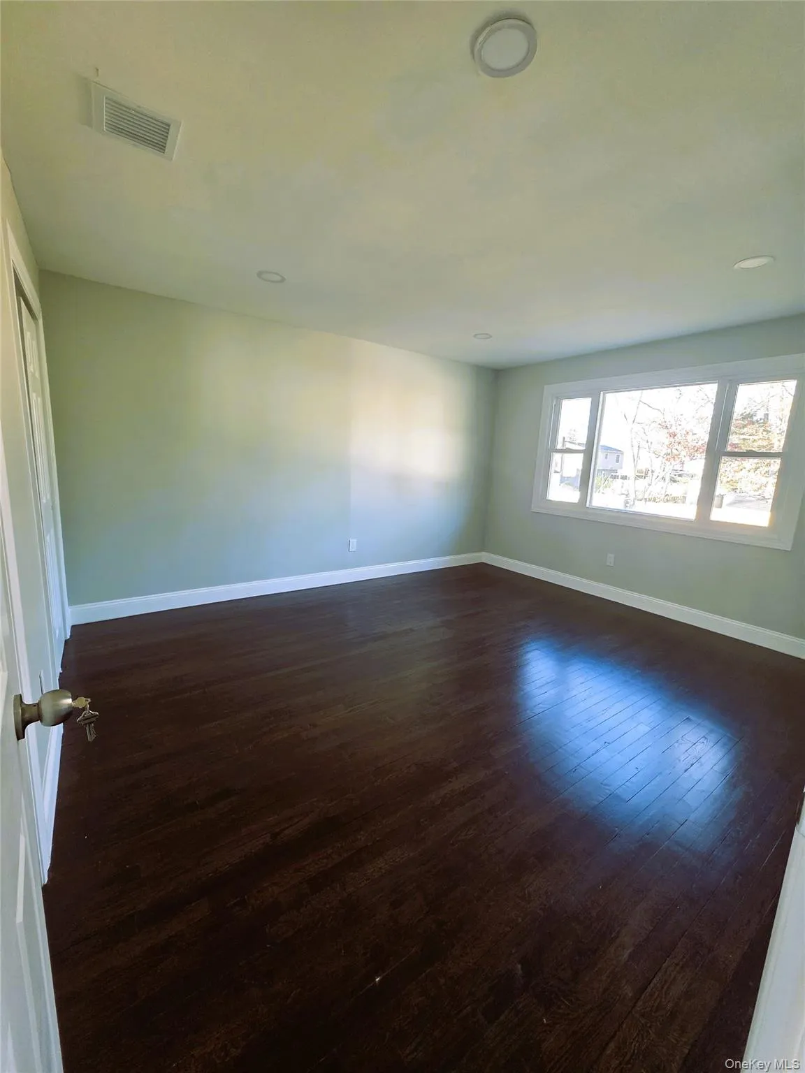 Spacious room featuring dark wood-finish flooring, white baseboards, and light-toned walls Spacious room featuring dark wood-finish flooring, white baseboards, and light-toned walls