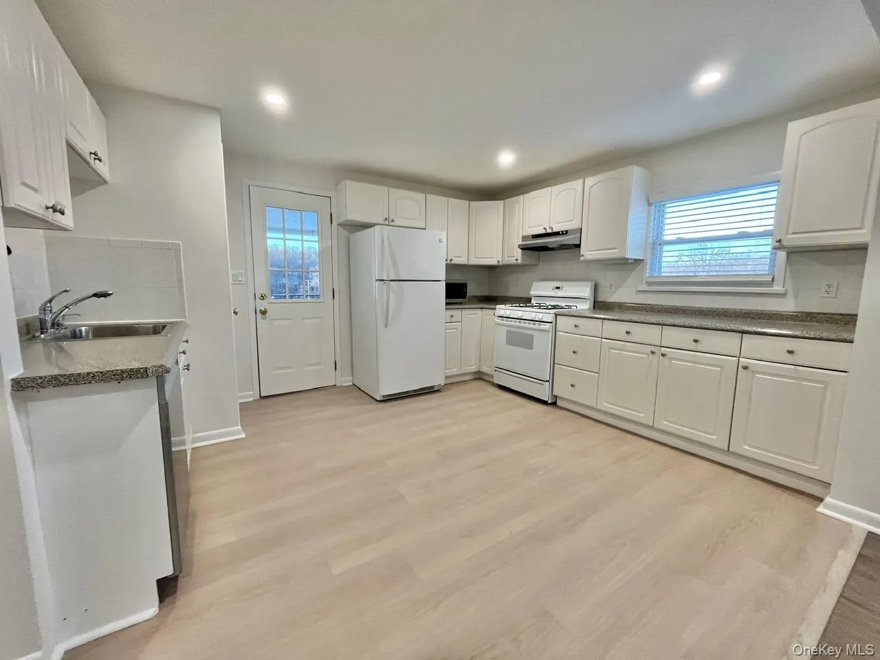 Kitchen featuring white cabinetry, white appliances, light wood-type flooring, under cabinet range hood, and recessed lighting Kitchen featuring white cabinetry, white appliances, light wood-type flooring, under cabinet range hood, and recessed lighting