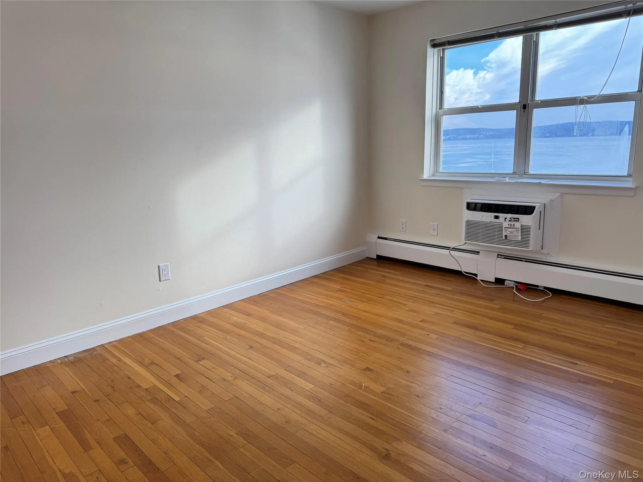 Bedroom #2 featuring light hard wood flooring, baseboard heating, and a wall unit AC Bedroom #2 featuring light hard wood flooring, baseboard heating, and a wall unit AC