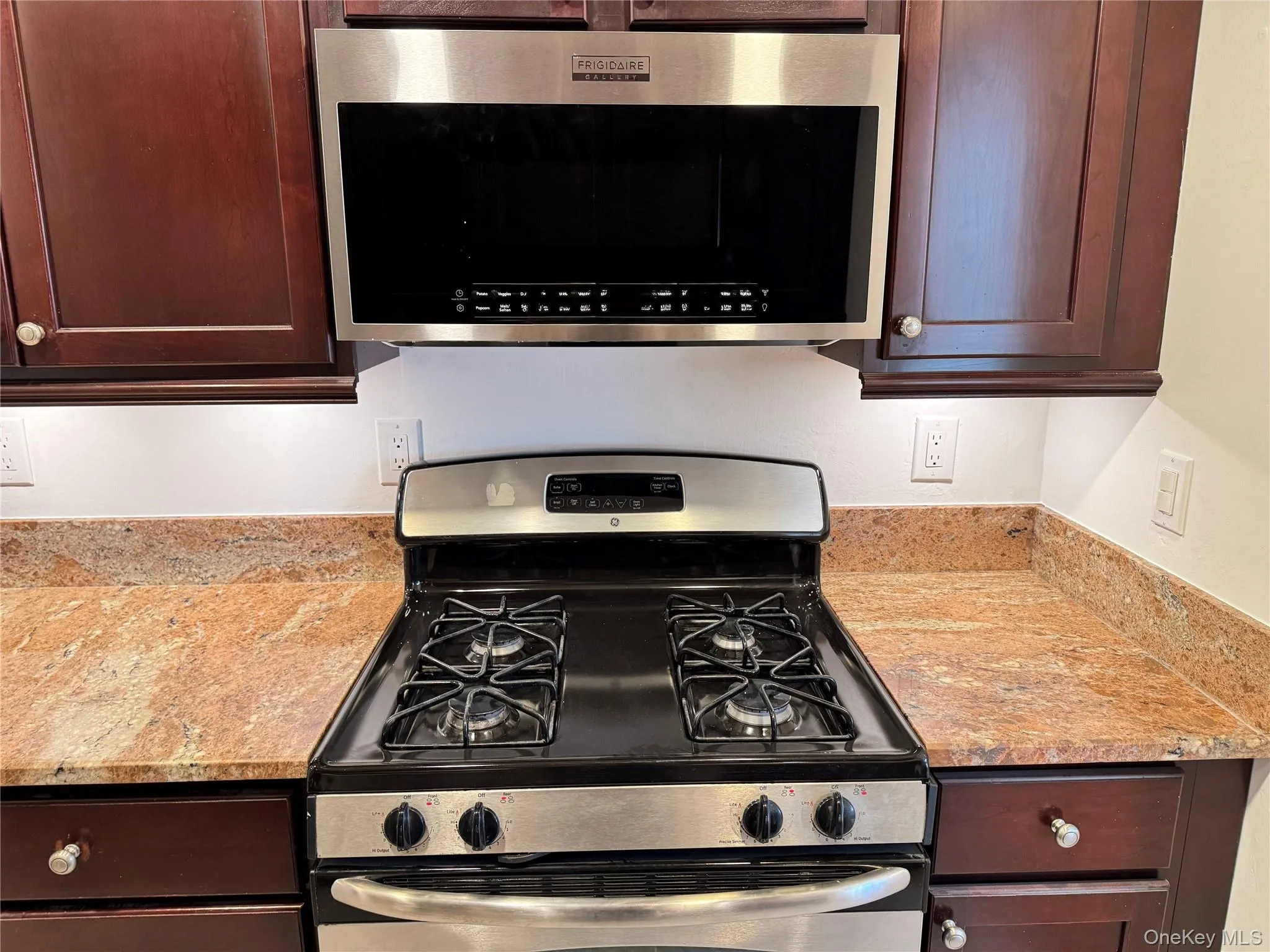 Kitchen featuring appliances with stainless steel finishes, light stone counters, and dark brown cabinetry Kitchen featuring appliances with stainless steel finishes, light stone counters, and dark brown cabinetry