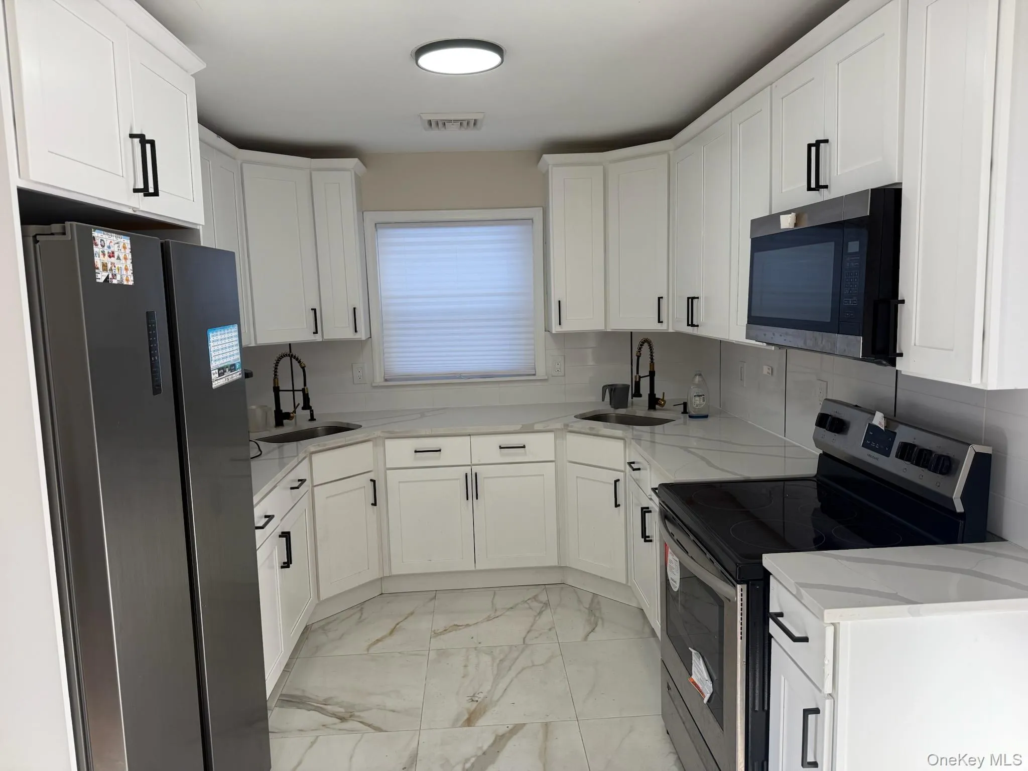 Kitchen featuring appliances with stainless steel finishes, light stone countertops, white cabinets, and light marble finish floors Kitchen featuring appliances with stainless steel finishes, light stone countertops, white cabinets, and light marble finish floors
