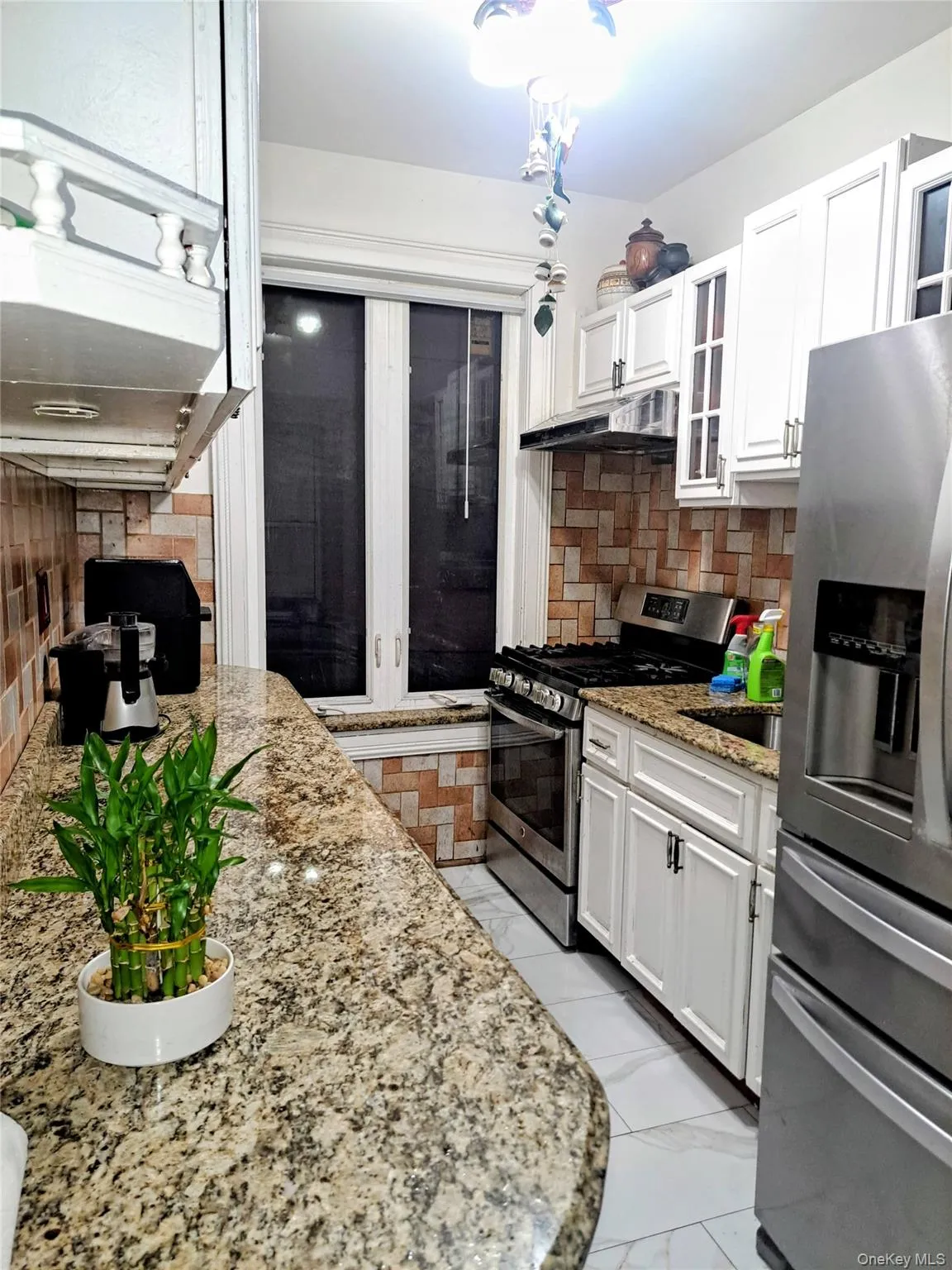 Kitchen featuring decorative backsplash, appliances with stainless steel finishes, light stone countertops, white cabinets, and under cabinet range hood Kitchen featuring decorative backsplash, appliances with stainless steel finishes, light stone countertops, white cabinets, and under cabinet range hood