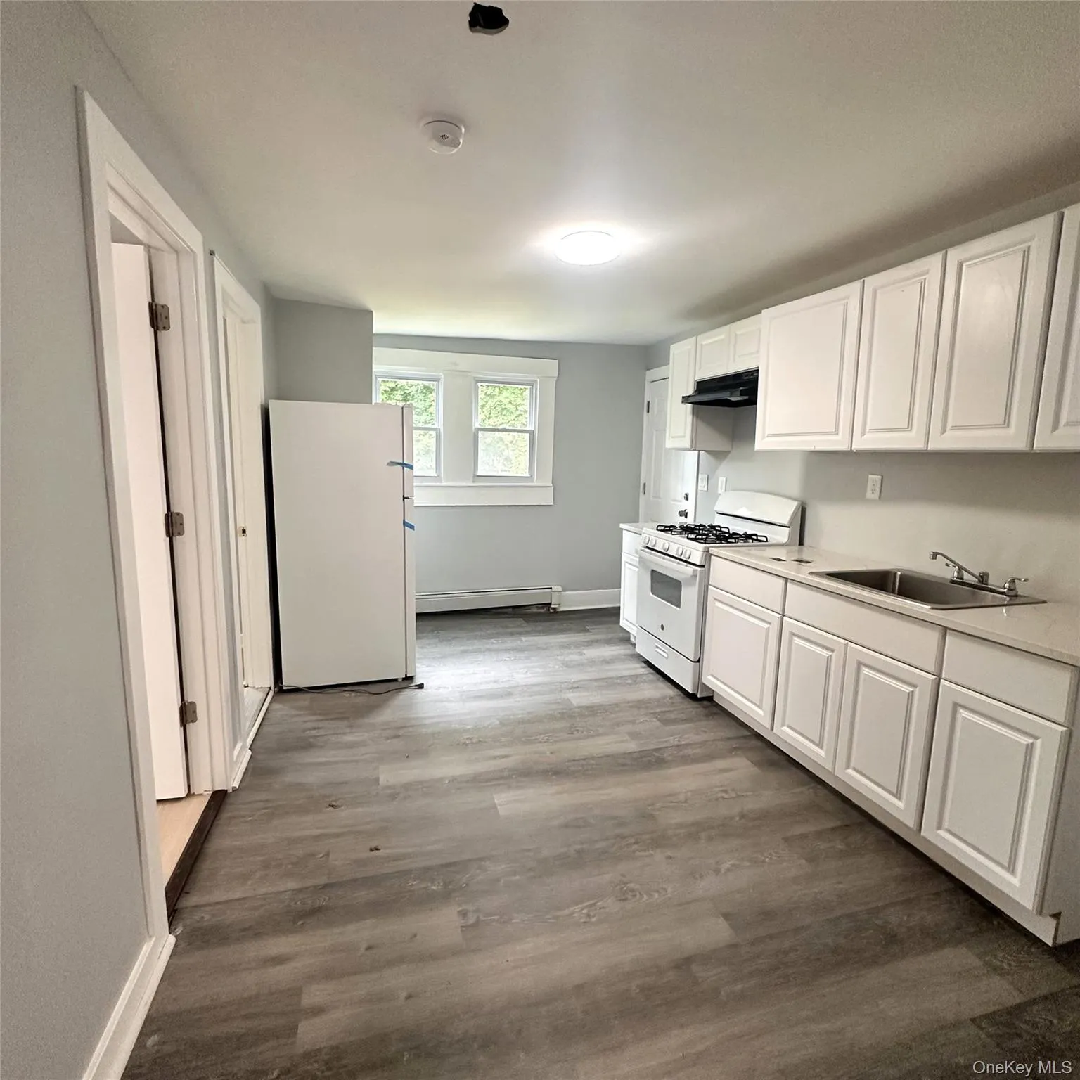 updated and modern kitchen featuring new white appliances, under cabinet range hood, a sink, and white cabinetry. Rear door to the back yard. updated and modern kitchen featuring new white appliances, under cabinet range hood, a sink, and white cabinetry. Rear door to the back yard.
