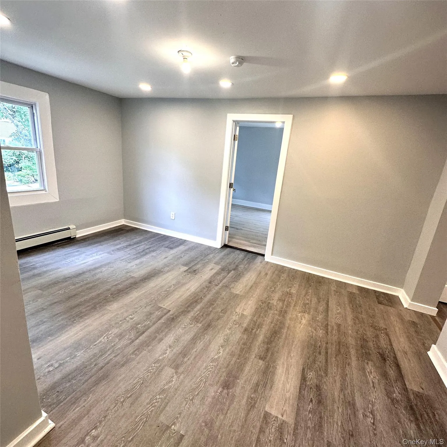 Unfurnished room with baseboard heating, baseboards, dark wood-type vinyl flooring, a smoke detector, and recessed lighting Unfurnished room with baseboard heating, baseboards, dark wood-type vinyl flooring, a smoke detector, and recessed lighting