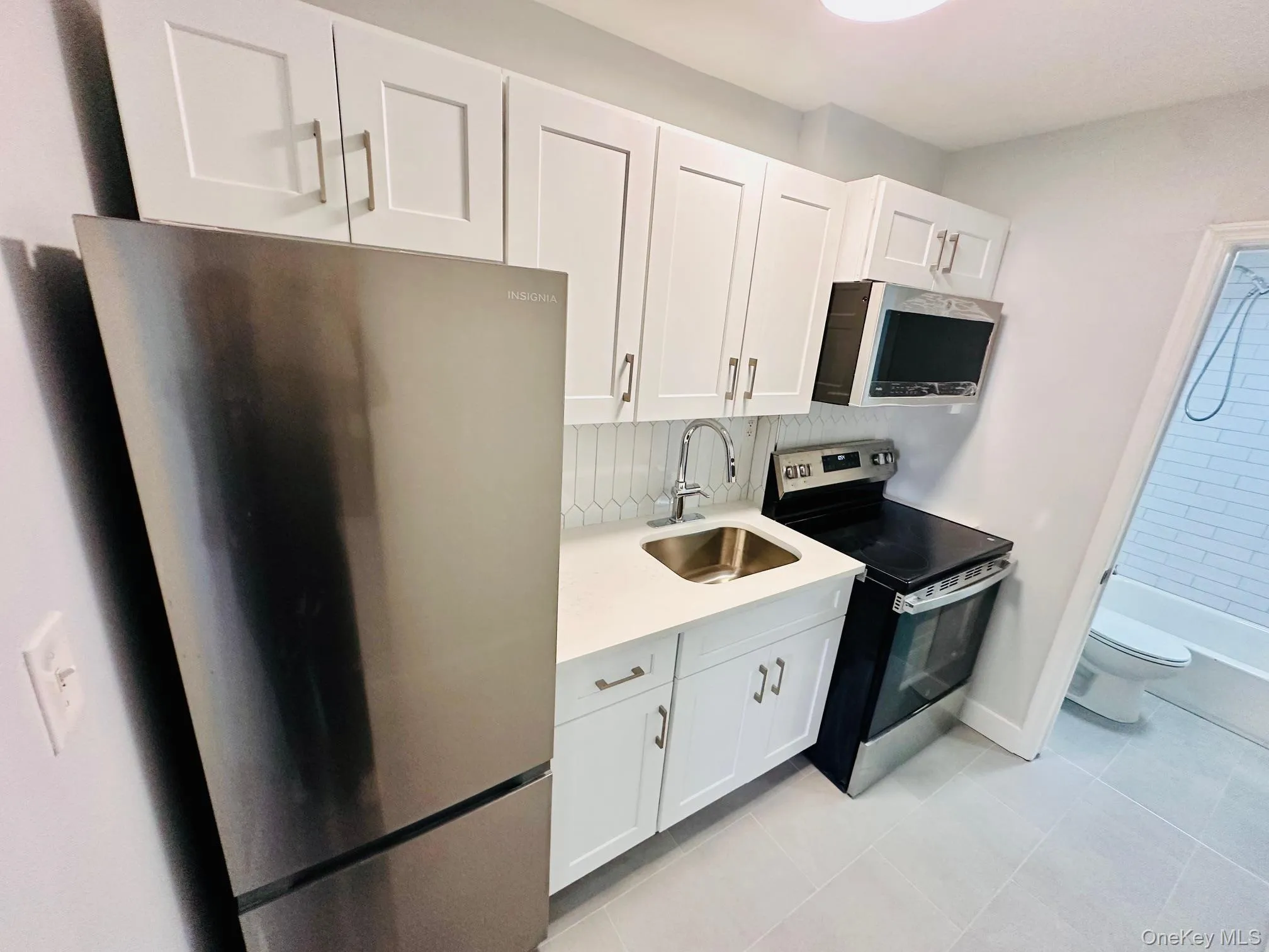 Kitchen with appliances with stainless steel finishes, white cabinets, light stone counters, and light tile patterned floors Kitchen with appliances with stainless steel finishes, white cabinets, light stone counters, and light tile patterned floors