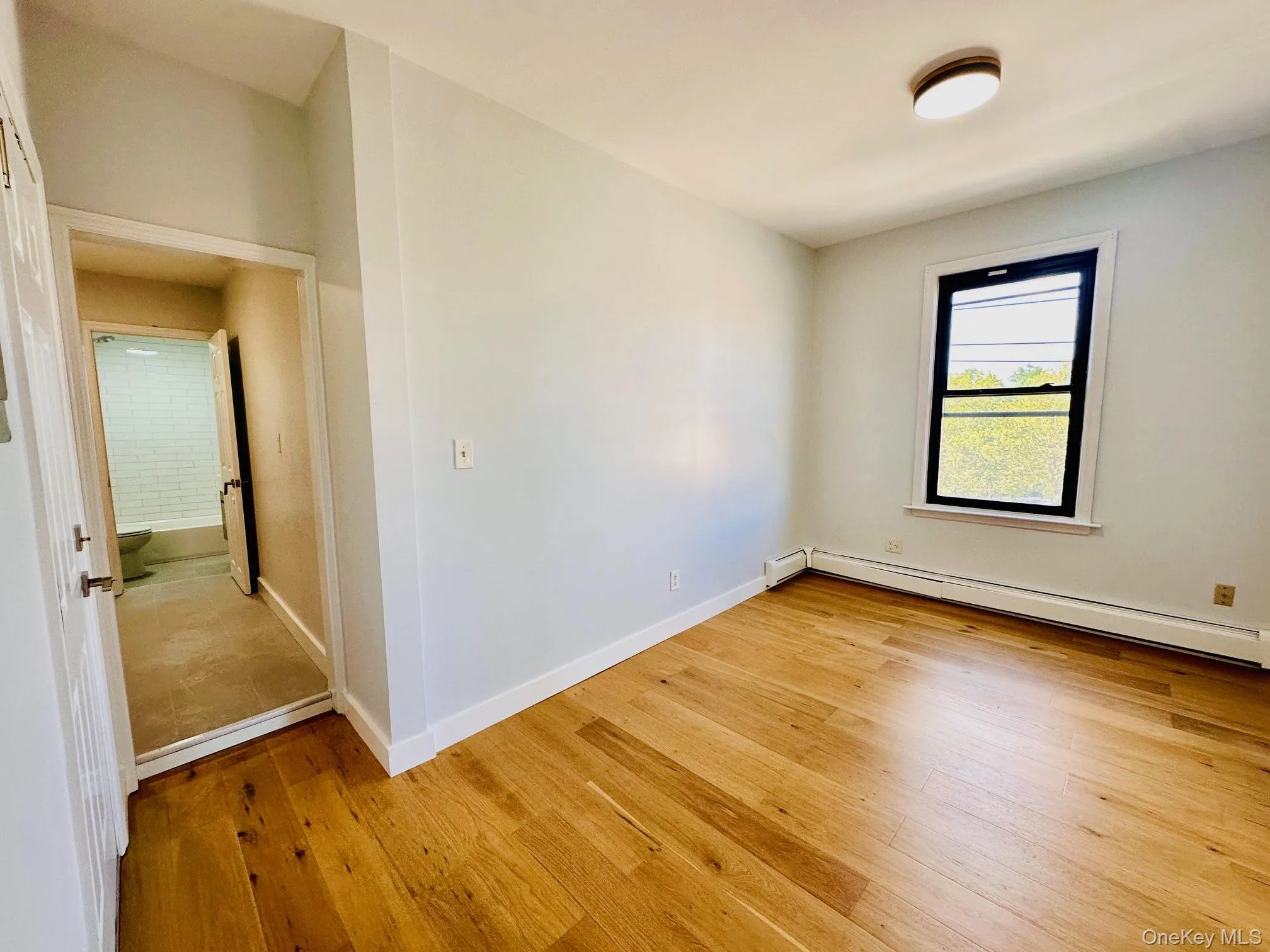 Unfurnished room with light wood finished floors and a baseboard heating unit Unfurnished room with light wood finished floors and a baseboard heating unit