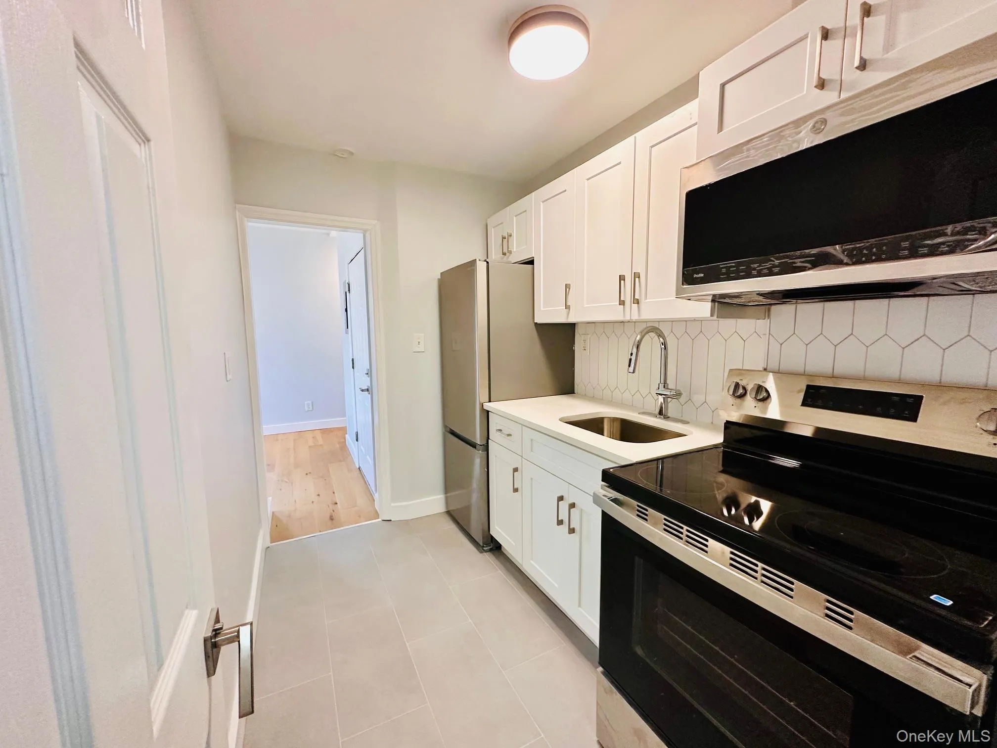 Kitchen featuring appliances with stainless steel finishes, white cabinets, tasteful backsplash, light tile patterned flooring, and light stone countertops Kitchen featuring appliances with stainless steel finishes, white cabinets, tasteful backsplash, light tile patterned flooring, and light stone countertops