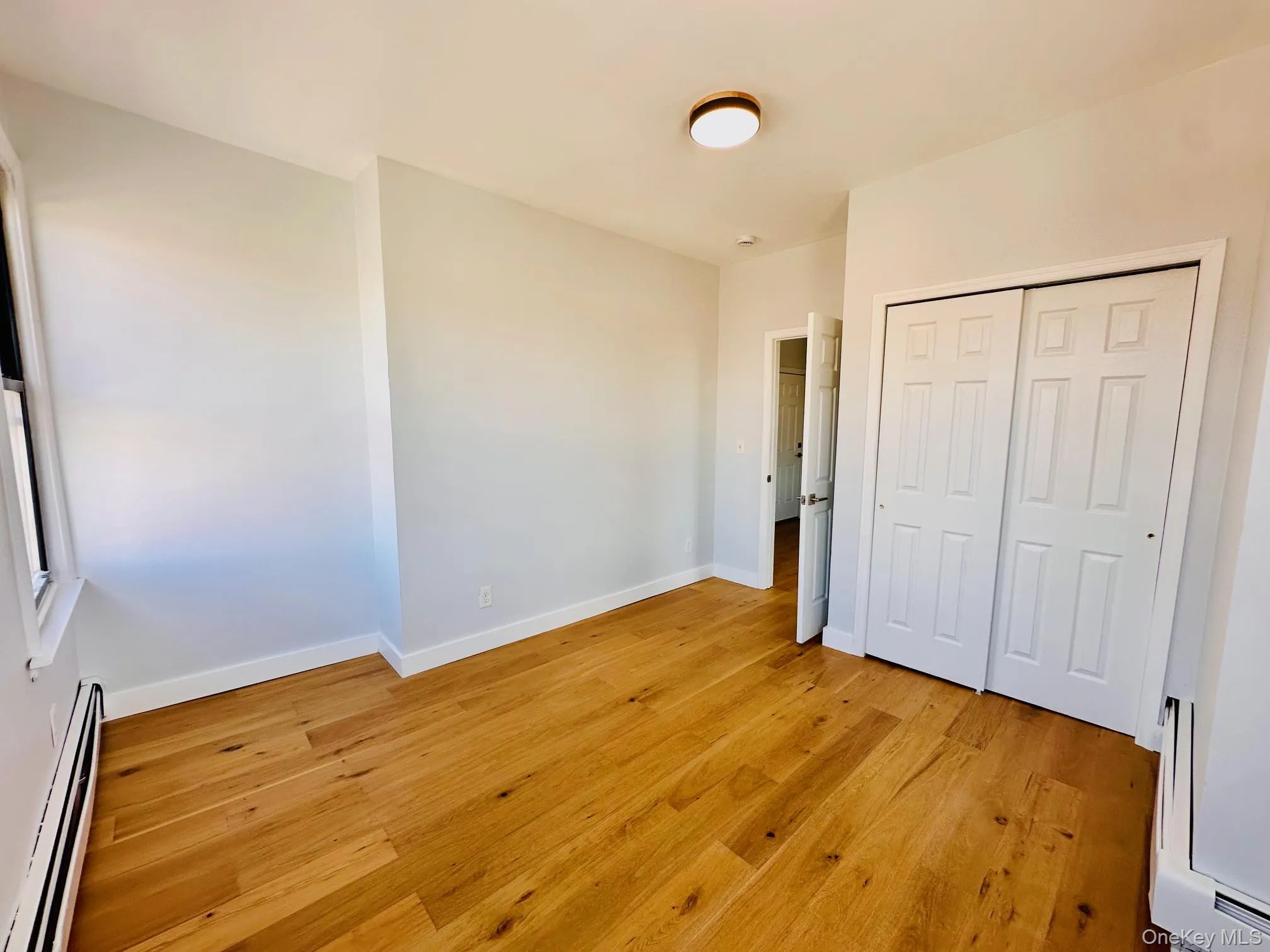 Unfurnished bedroom with a baseboard heating unit, light wood-style flooring, and a closet Unfurnished bedroom with a baseboard heating unit, light wood-style flooring, and a closet