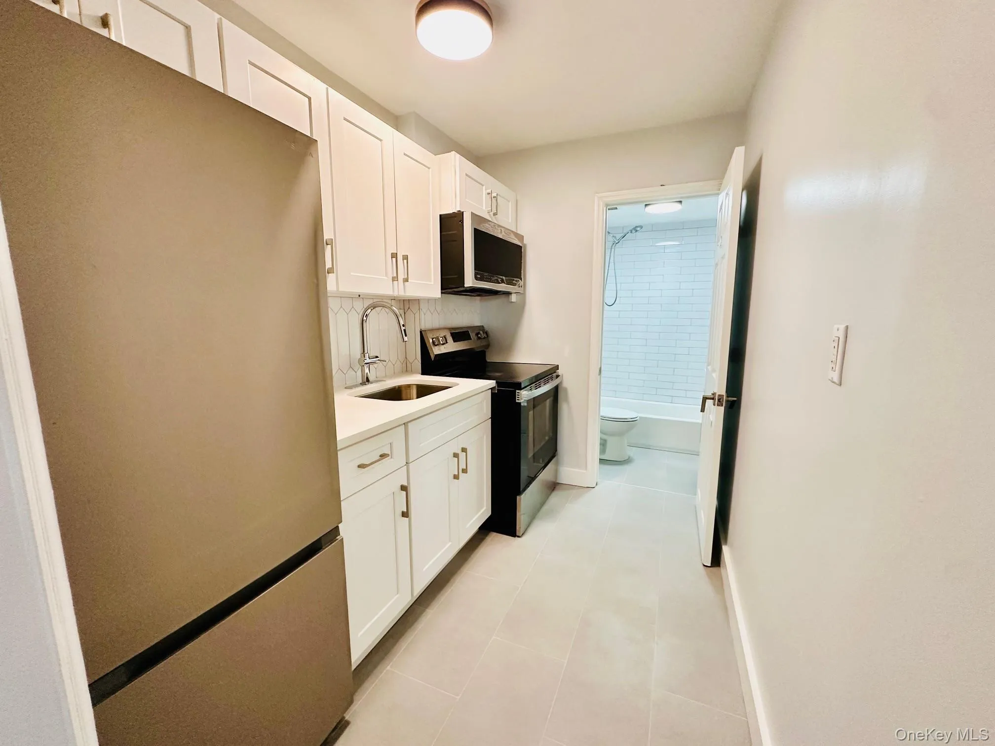 Kitchen featuring stainless steel appliances, white cabinets, decorative backsplash, and light tile patterned flooring Kitchen featuring stainless steel appliances, white cabinets, decorative backsplash, and light tile patterned flooring