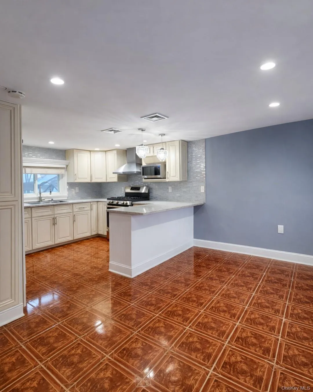 Kitchen with wall chimney range hood, decorative backsplash, a peninsula, stainless steel microwave, and light stone counters Kitchen with wall chimney range hood, decorative backsplash, a peninsula, stainless steel microwave, and light stone counters