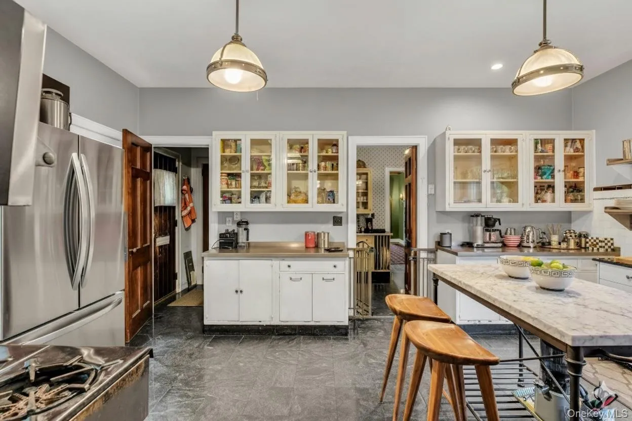 Kitchen with white cabinets, appliances with stainless steel finishes, glass insert cabinets, open shelves, and hanging light fixtures Kitchen with white cabinets, appliances with stainless steel finishes, glass insert cabinets, open shelves, and hanging light fixtures