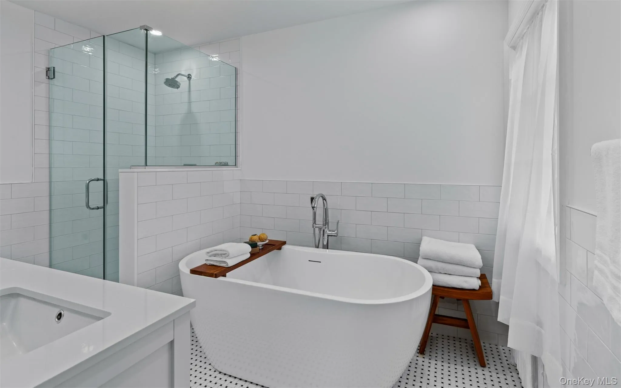 White subway tile, glass-enclosed shower, freestanding soaking tub, single vanity with integrated sink, and hexagon mosaic floor tile White subway tile, glass-enclosed shower, freestanding soaking tub, single vanity with integrated sink, and hexagon mosaic floor tile