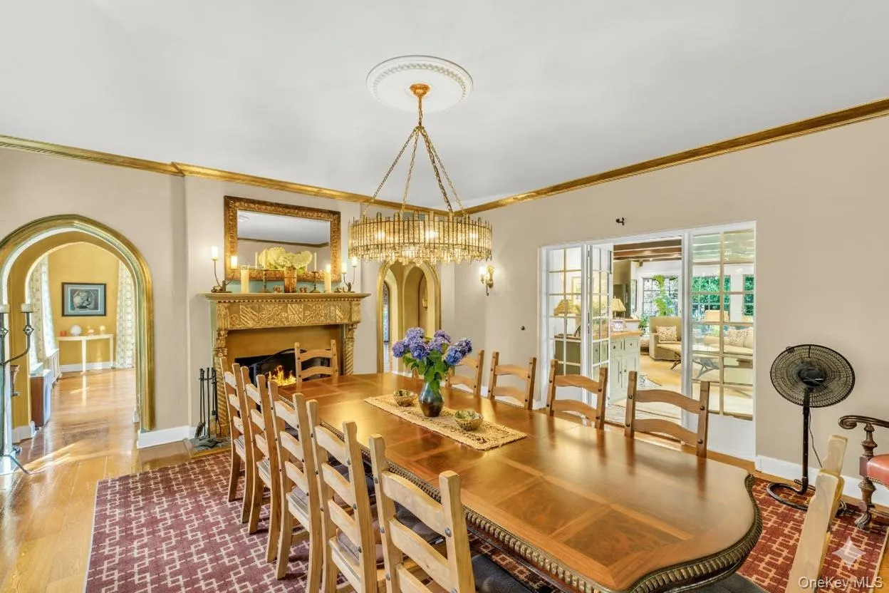 Dining space featuring ornamental molding, arched walkways, wood finished floors, and a lit fireplace Dining space featuring ornamental molding, arched walkways, wood finished floors, and a lit fireplace