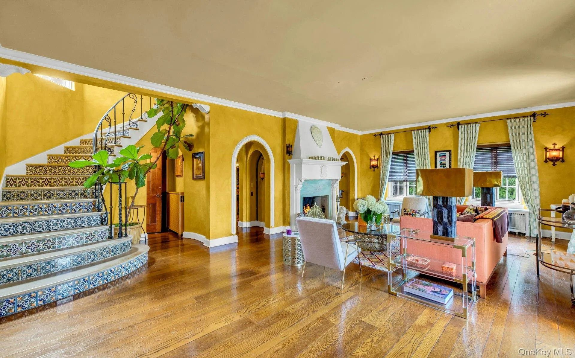 Entering formal living room from center hall, featuring terra cotta tile princess staircase, floor to ceiling fireplace, 9.5 ft ceilings, solid wood floors, crown molding, and archways to formal dining room, 2 french doors to front patio Entering formal living room from center hall, featuring terra cotta tile princess staircase, floor to ceiling fireplace, 9.5 ft ceilings, solid wood floors, crown molding, and archways to formal dining room, 2 french doors to front patio