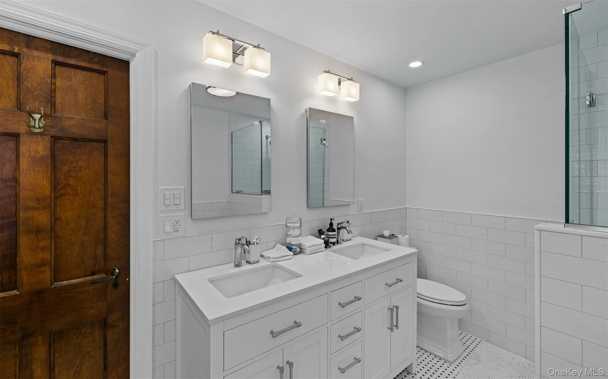 Brand new primary bath w/Dual vanity with integrated sinks and chrome fixtures, subway tile wainscoting, white hex tile flooring, and a glass-enclosed shower Brand new primary bath w/Dual vanity with integrated sinks and chrome fixtures, subway tile wainscoting, white hex tile flooring, and a glass-enclosed shower