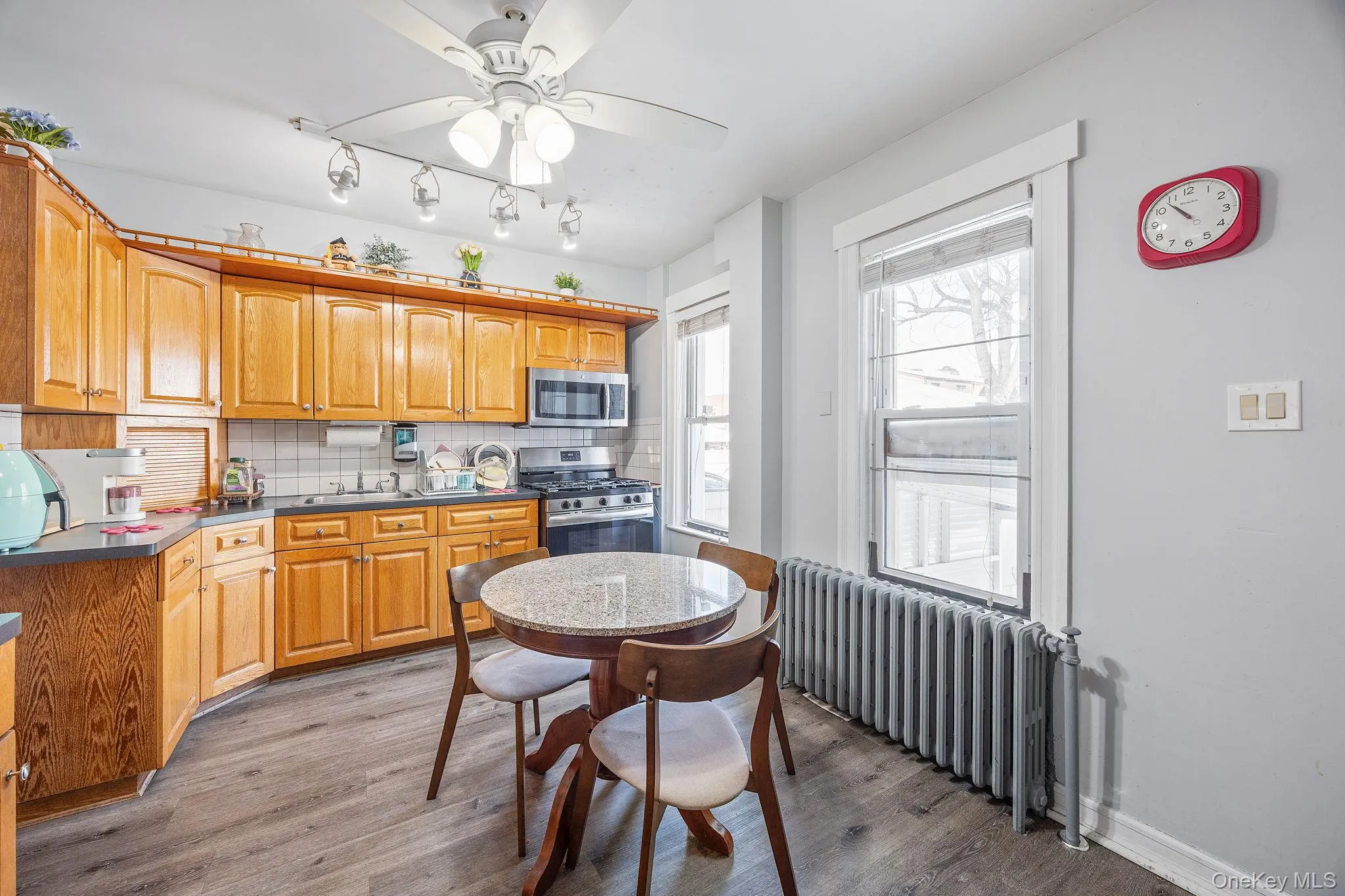 Kitchen featuring radiator, stainless steel appliances, dark wood finished floors, a ceiling fan, and dark countertops Kitchen featuring radiator, stainless steel appliances, dark wood finished floors, a ceiling fan, and dark countertops