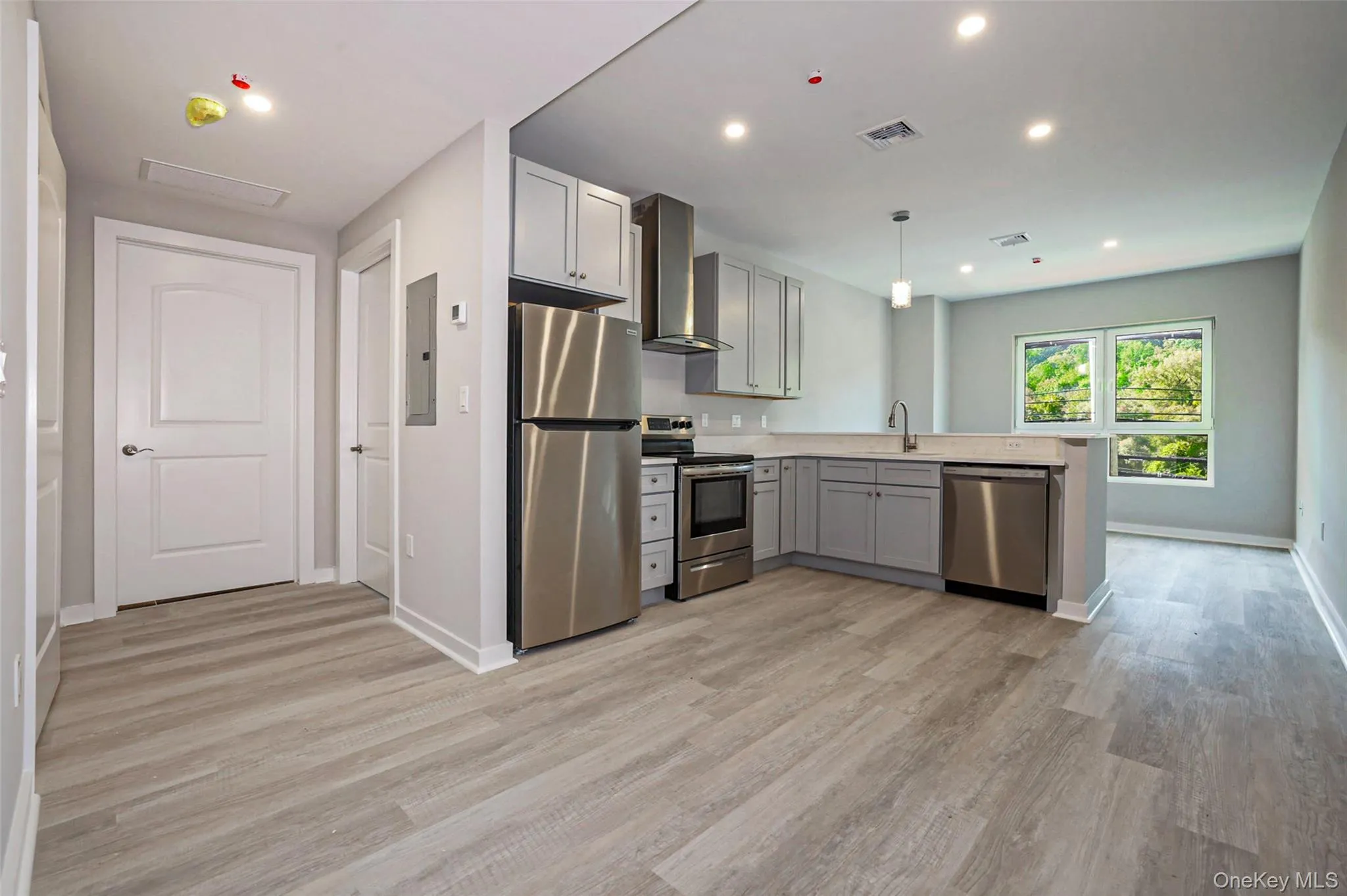Kitchen featuring stainless steel appliances, light countertops, gray cabinets, wall chimney exhaust hood, and pendant lighting Kitchen featuring stainless steel appliances, light countertops, gray cabinets, wall chimney exhaust hood, and pendant lighting
