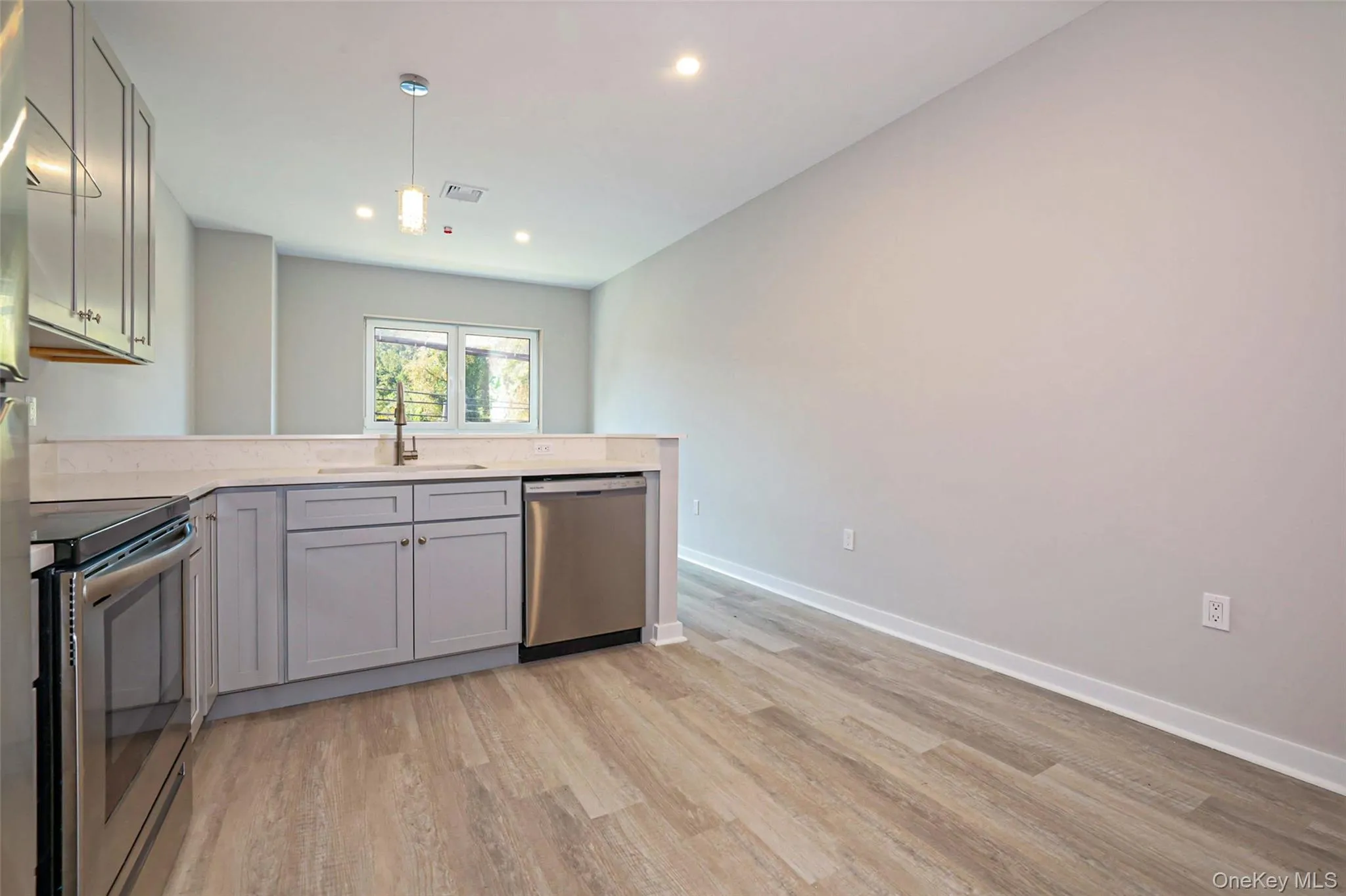 Kitchen featuring stainless steel appliances, gray cabinets, light wood-style flooring, a peninsula, and pendant lighting Kitchen featuring stainless steel appliances, gray cabinets, light wood-style flooring, a peninsula, and pendant lighting