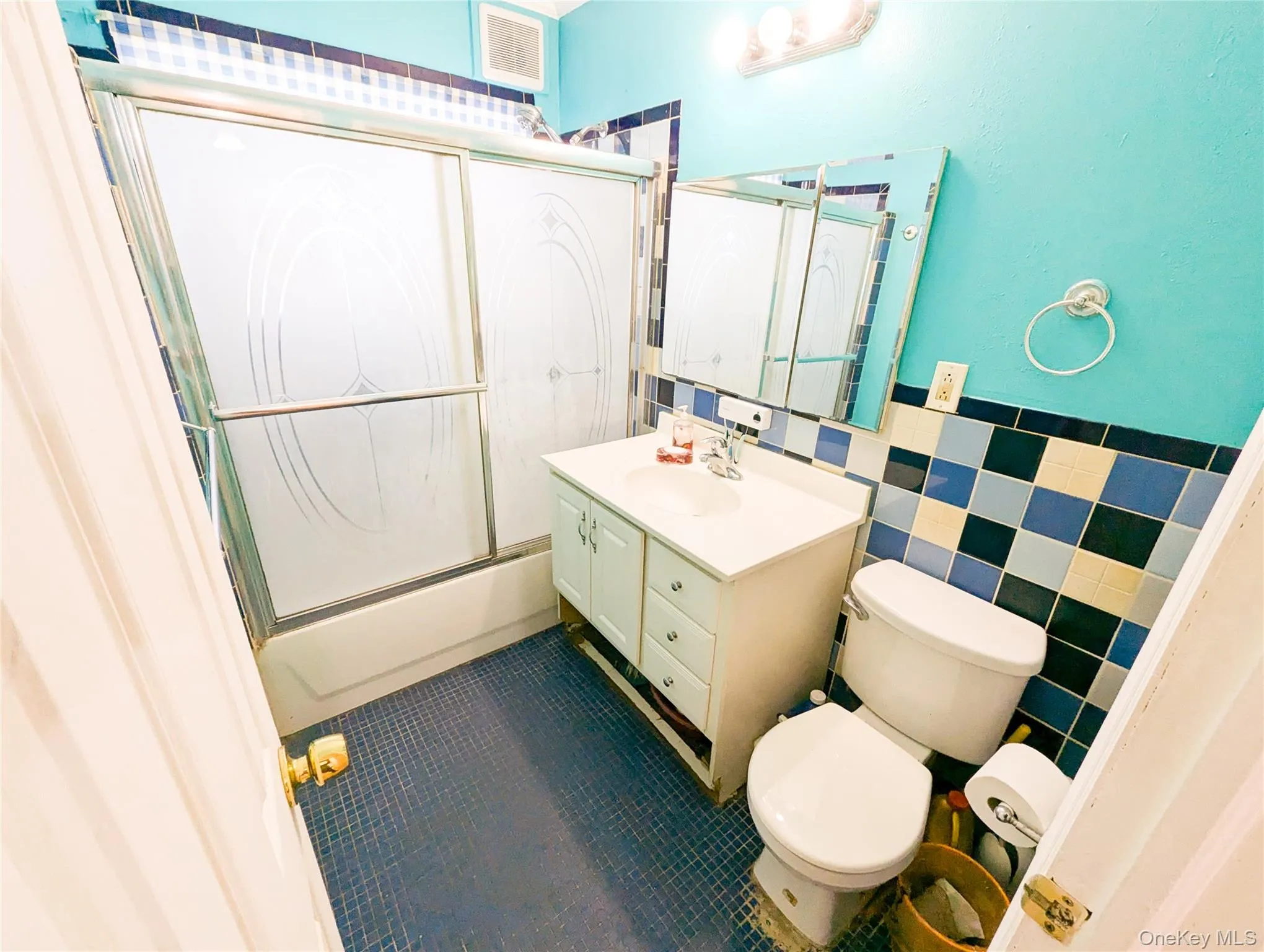 Full bathroom with tile patterned floors, vanity, shower / bath combination with glass door, tile walls, and toilet Full bathroom with tile patterned floors, vanity, shower / bath combination with glass door, tile walls, and toilet