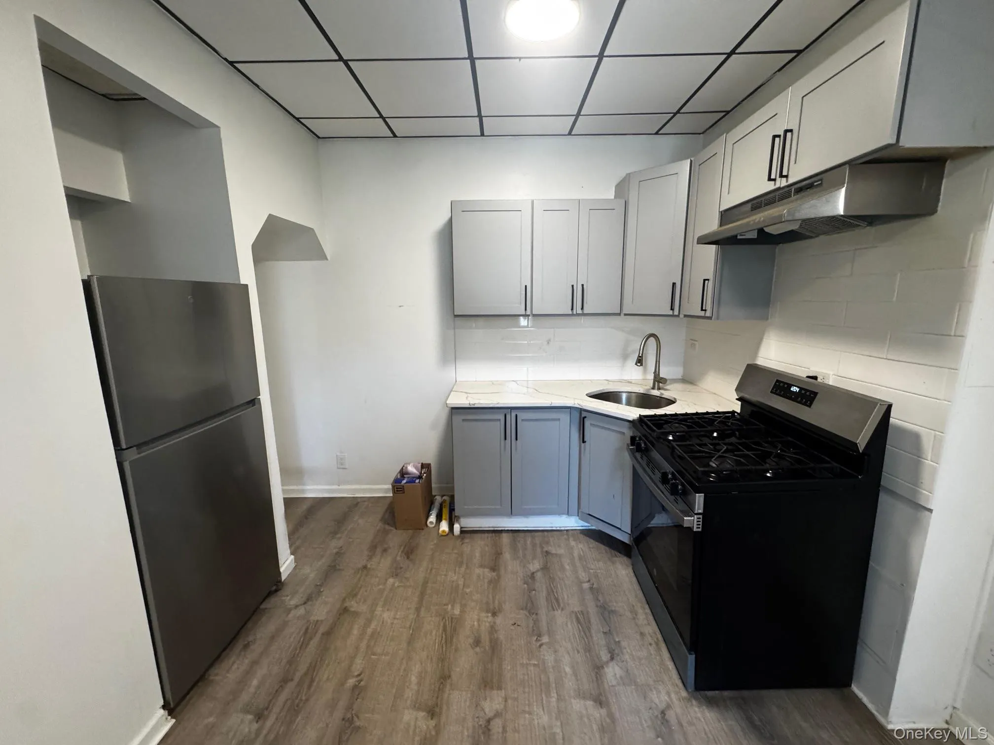 Kitchen featuring gray cabinetry, gas stove, freestanding refrigerator, and under cabinet range hood Kitchen featuring gray cabinetry, gas stove, freestanding refrigerator, and under cabinet range hood