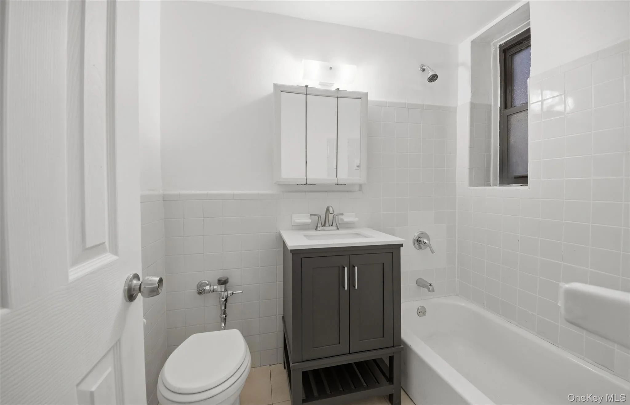 Fully renovated full bathroom featuring bathtub / shower combination, vanity, tile walls, light tile patterned floors, and wainscoting Fully renovated full bathroom featuring bathtub / shower combination, vanity, tile walls, light tile patterned floors, and wainscoting