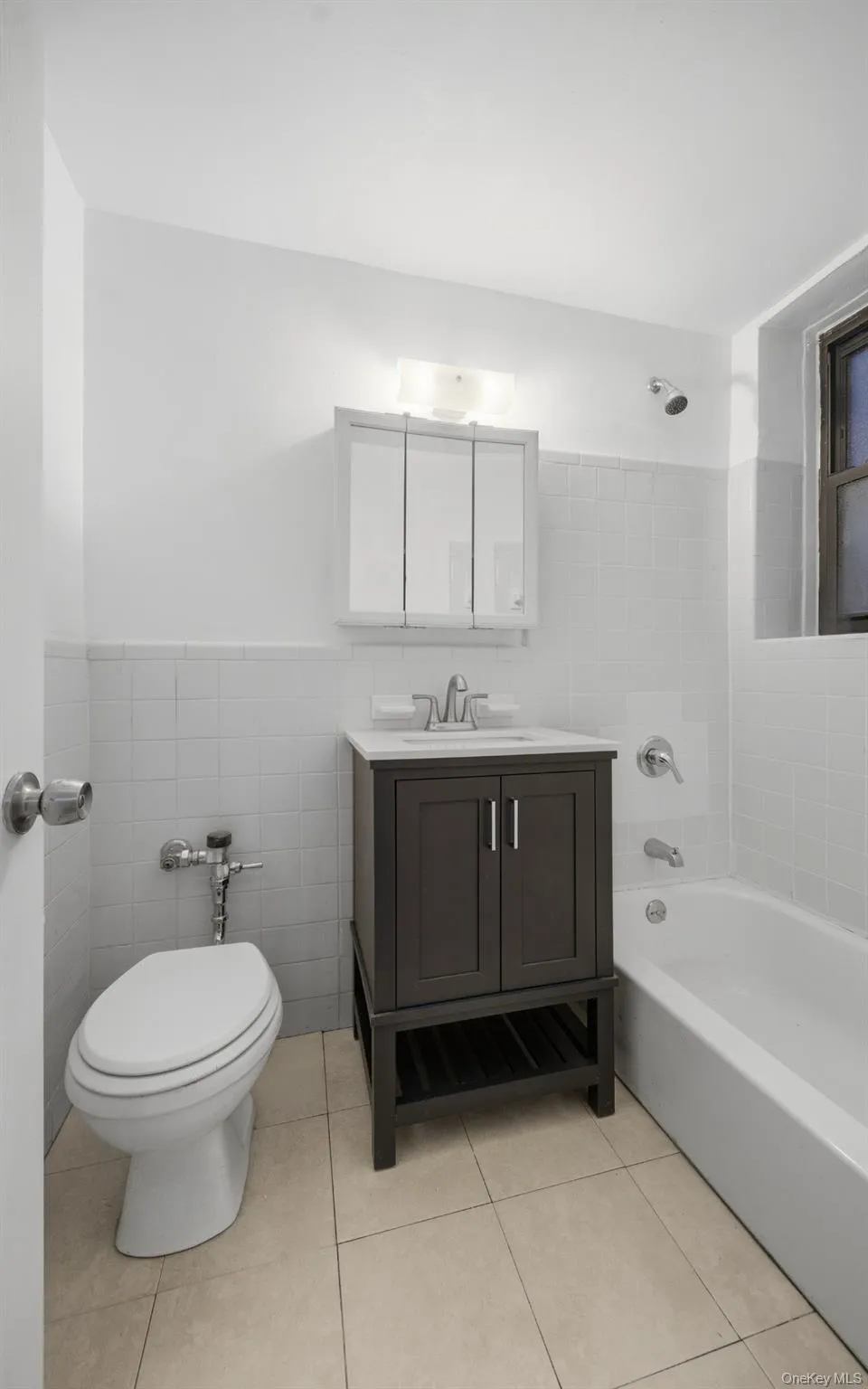 Fully renovated full bathroom featuring bathtub / shower combination, vanity, tile walls, light tile patterned floors, and wainscoting Fully renovated full bathroom featuring bathtub / shower combination, vanity, tile walls, light tile patterned floors, and wainscoting