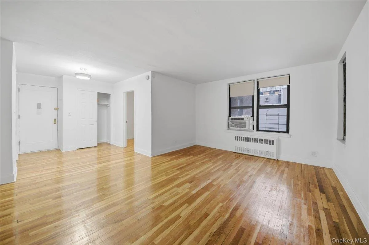 Living/Bedroom area featuring light wood finished floors, radiator heating unit, and cooling unit Living/Bedroom area featuring light wood finished floors, radiator heating unit, and cooling unit