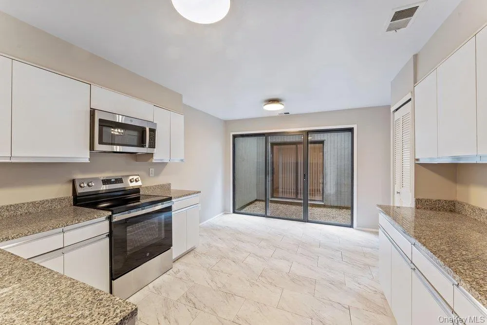 Kitchen featuring white cabinets, stainless steel appliances, and light stone countertops Kitchen featuring white cabinets, stainless steel appliances, and light stone countertops