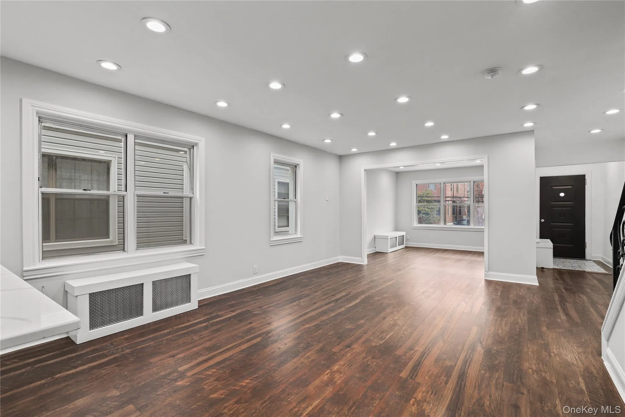 Unfurnished living room with radiator, dark wood-style flooring, and recessed lighting Unfurnished living room with radiator, dark wood-style flooring, and recessed lighting