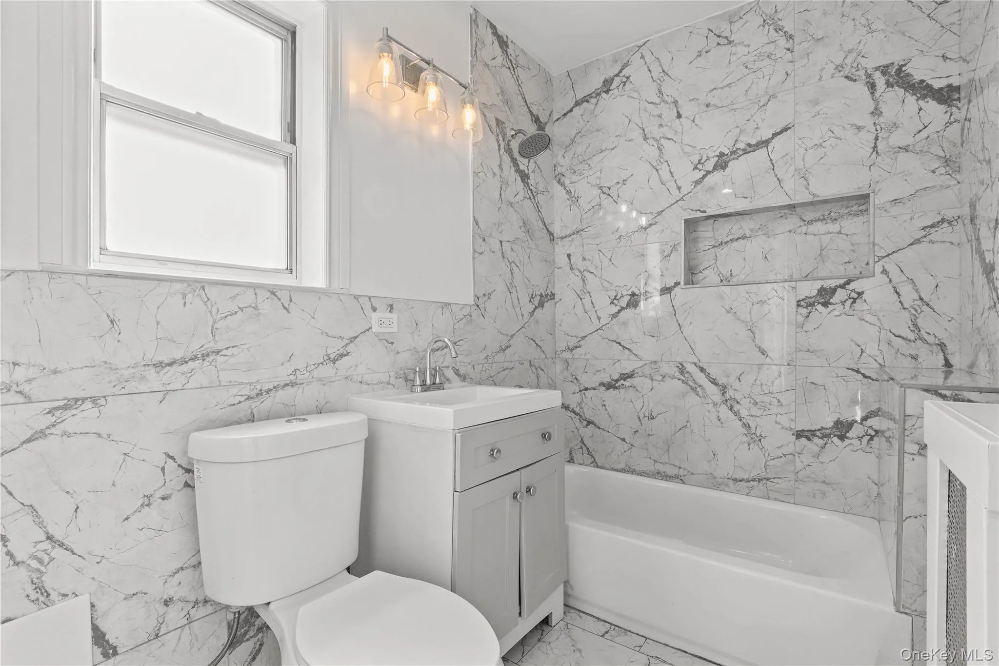 Full bath with bathing tub / shower combination, vanity, tile walls, and light marble finish floors Full bath with bathing tub / shower combination, vanity, tile walls, and light marble finish floors
