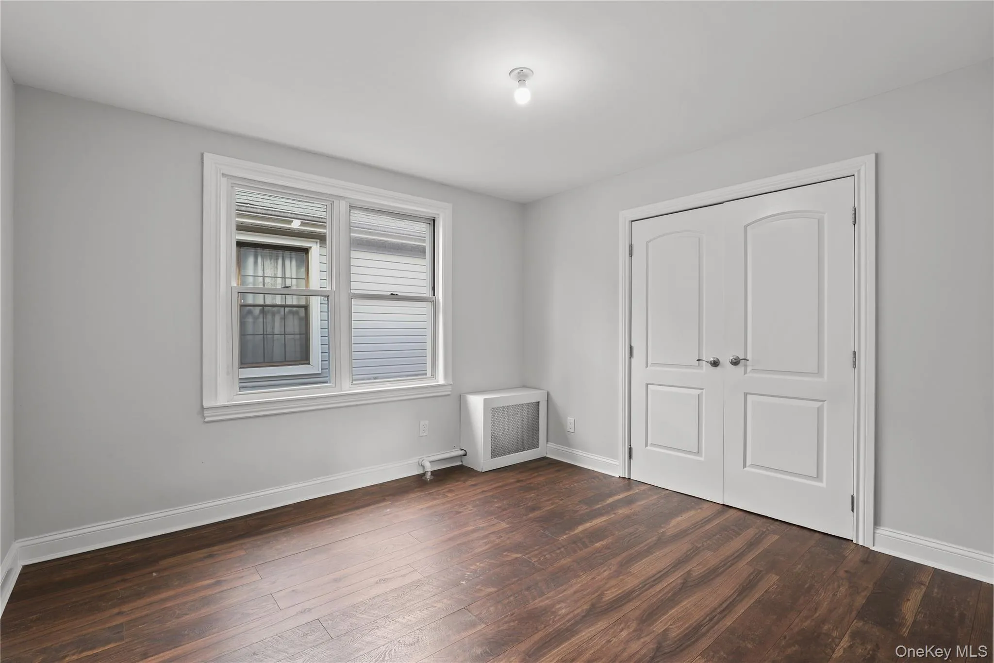 Unfurnished bedroom with dark wood-type flooring, radiator, and a closet Unfurnished bedroom with dark wood-type flooring, radiator, and a closet