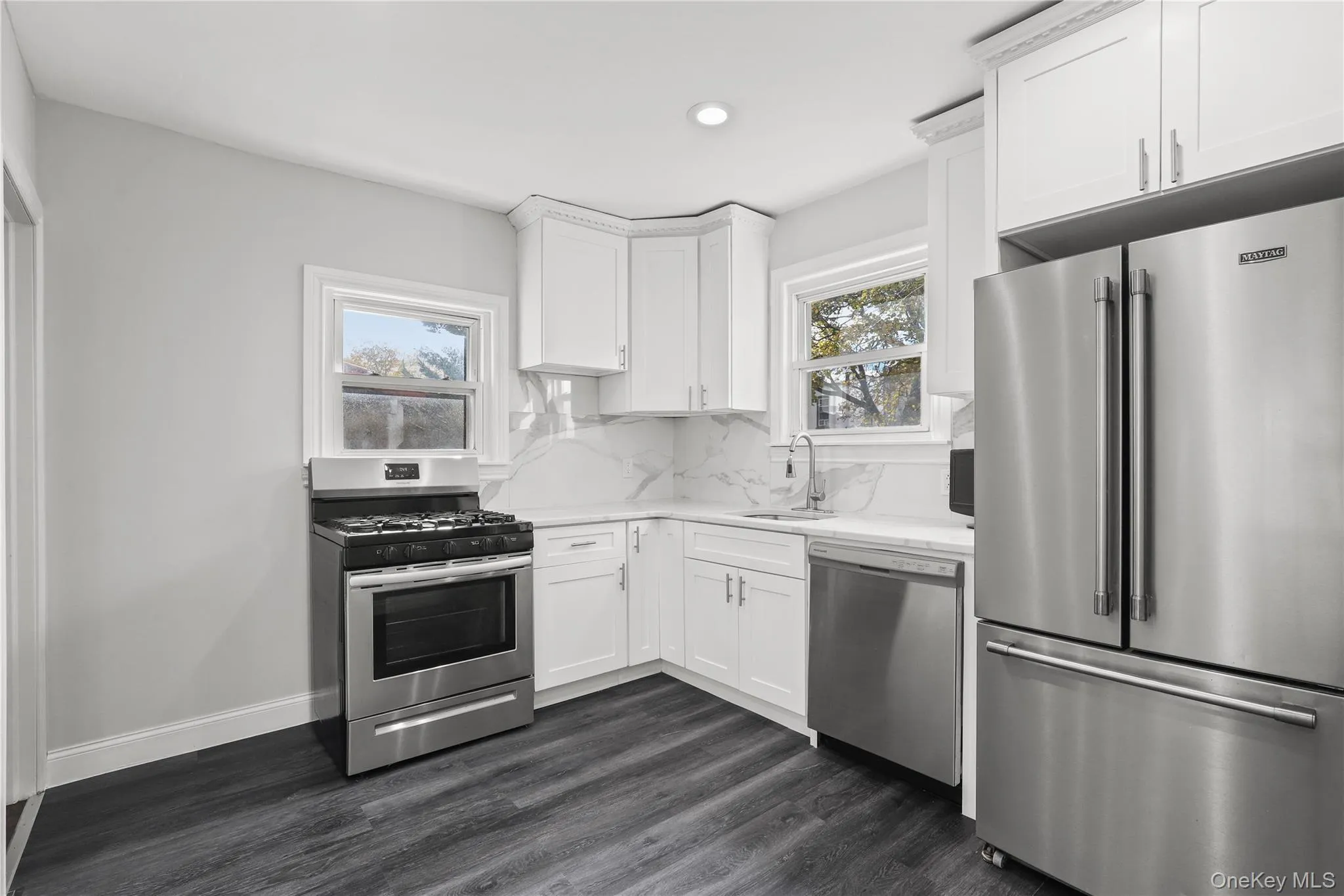 Kitchen with stainless steel appliances, dark wood finished floors, white cabinets, decorative backsplash, and recessed lighting Kitchen with stainless steel appliances, dark wood finished floors, white cabinets, decorative backsplash, and recessed lighting