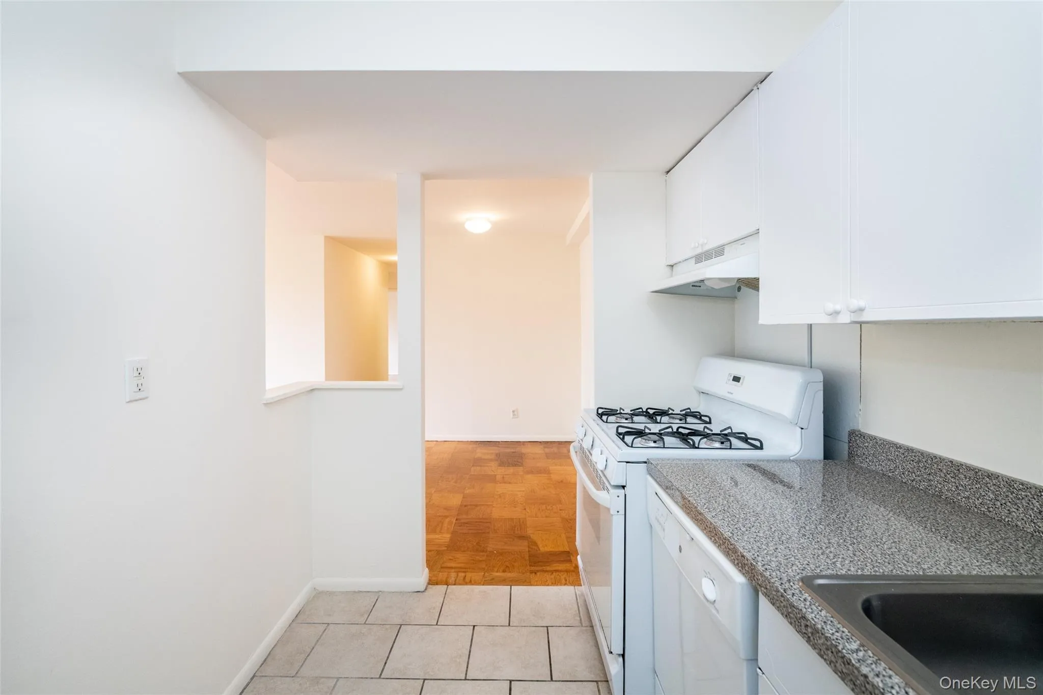 Kitchen featuring white appliances, white cabinets, under cabinet range hood, and light tile patterned floors Kitchen featuring white appliances, white cabinets, under cabinet range hood, and light tile patterned floors