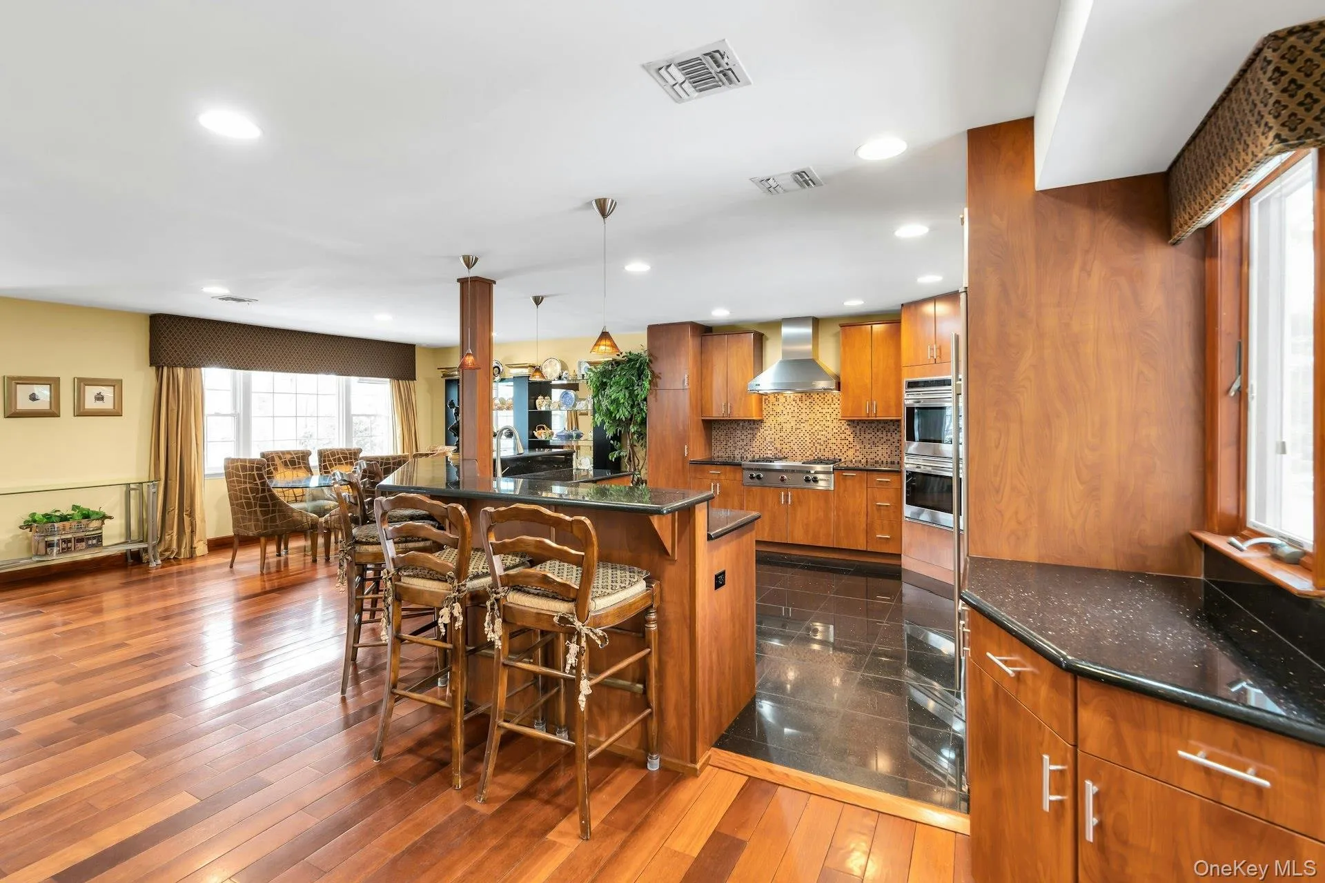 Kitchen with wood finish cabinetry, a kitchen breakfast bar, dark stone counters, hanging light fixtures, and stainless steel appliances Kitchen with wood finish cabinetry, a kitchen breakfast bar, dark stone counters, hanging light fixtures, and stainless steel appliances