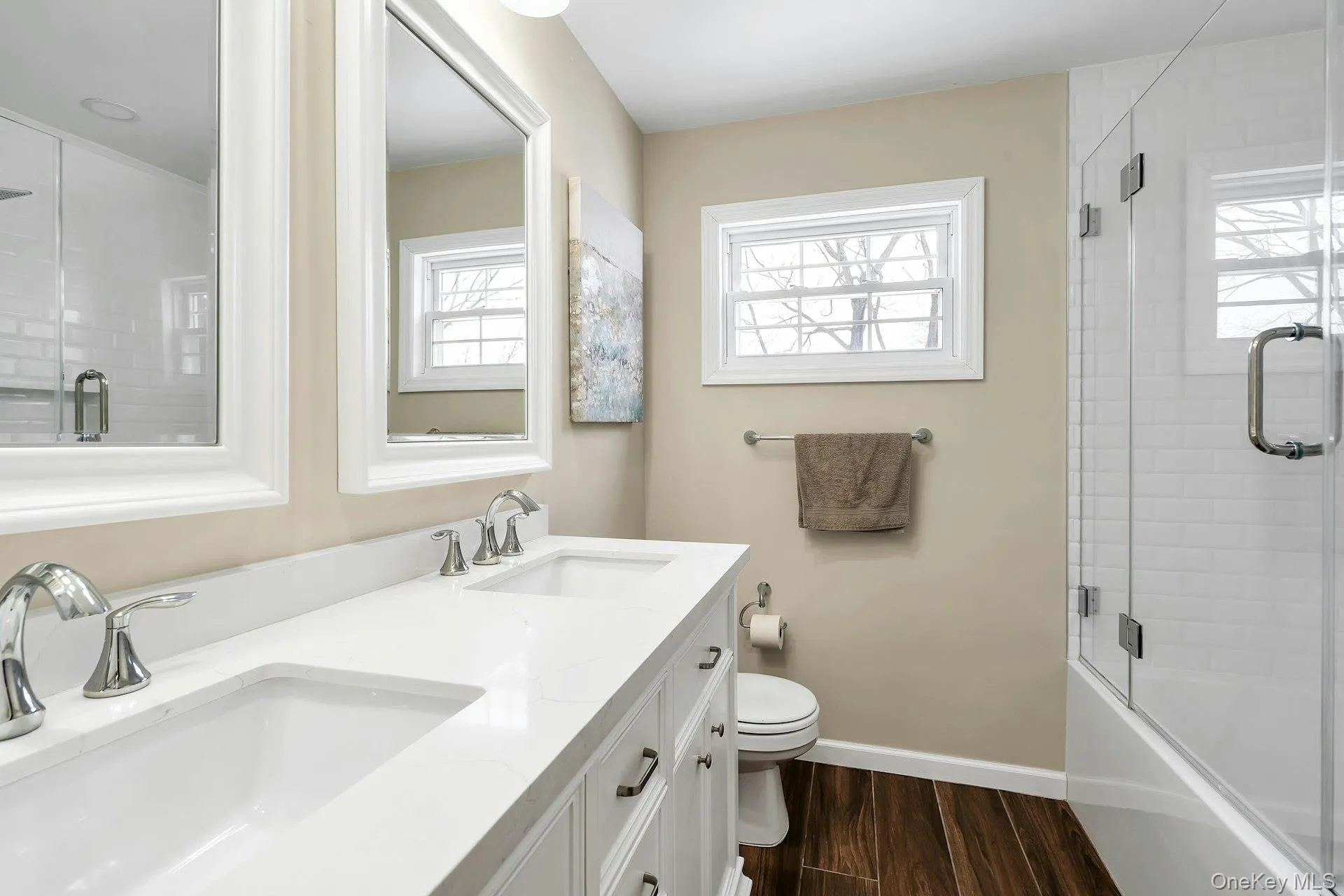Bathroom featuring double vanity, shower / bath combination with glass door, and dark wood finished floors Bathroom featuring double vanity, shower / bath combination with glass door, and dark wood finished floors