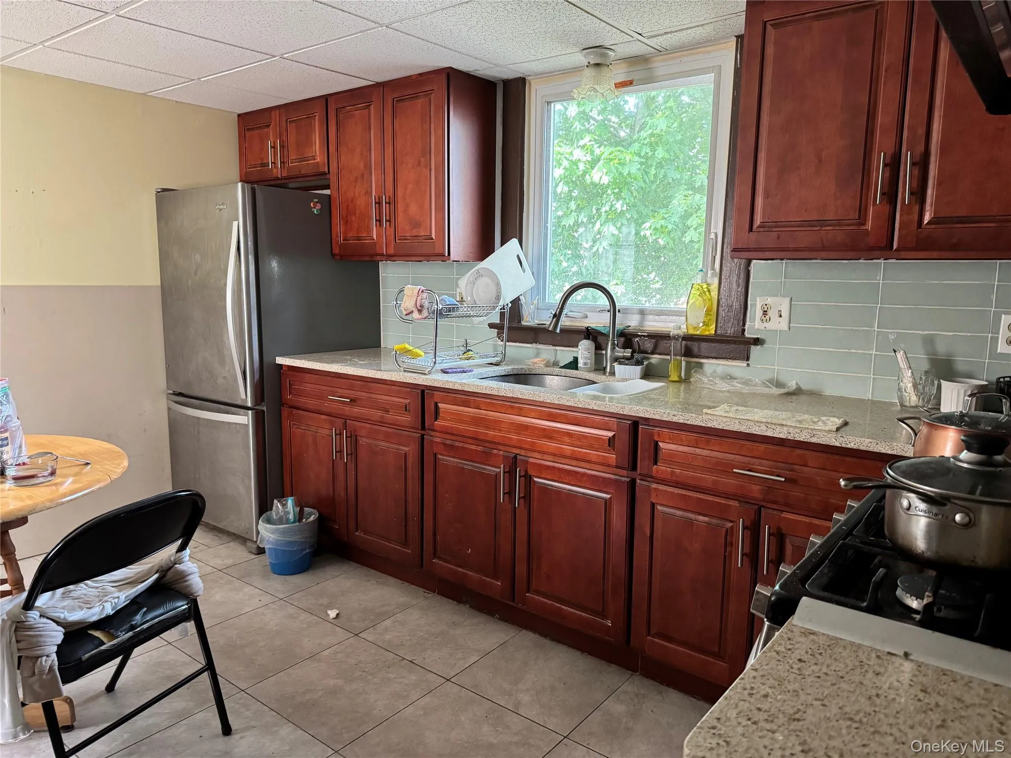Kitchen with a sink, freestanding refrigerator, tasteful backsplash, gas stove, and a paneled ceiling Kitchen with a sink, freestanding refrigerator, tasteful backsplash, gas stove, and a paneled ceiling