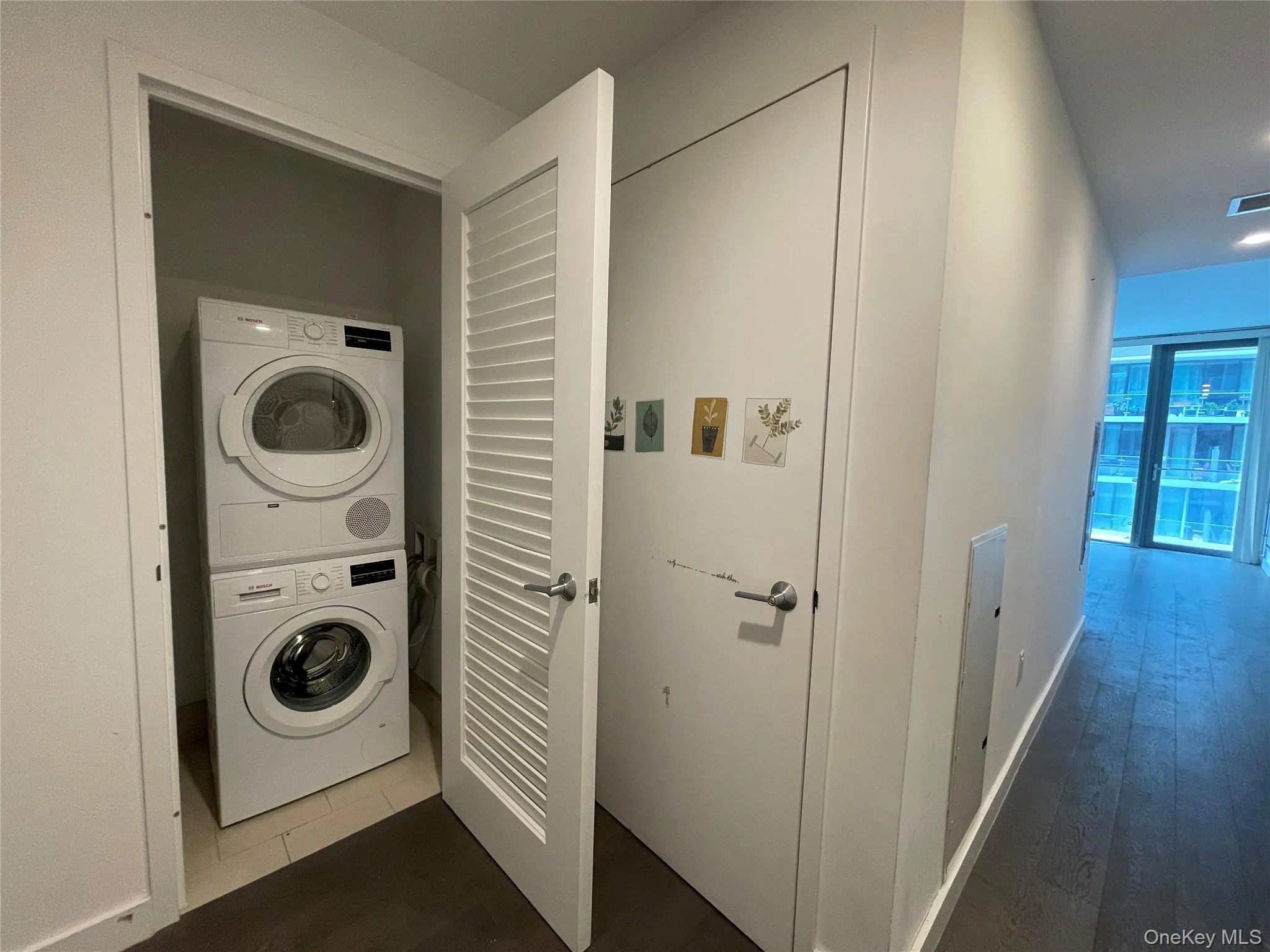 Laundry area with stacked washer and clothes dryer, dark wood-style floors, and recessed lighting Laundry area with stacked washer and clothes dryer, dark wood-style floors, and recessed lighting