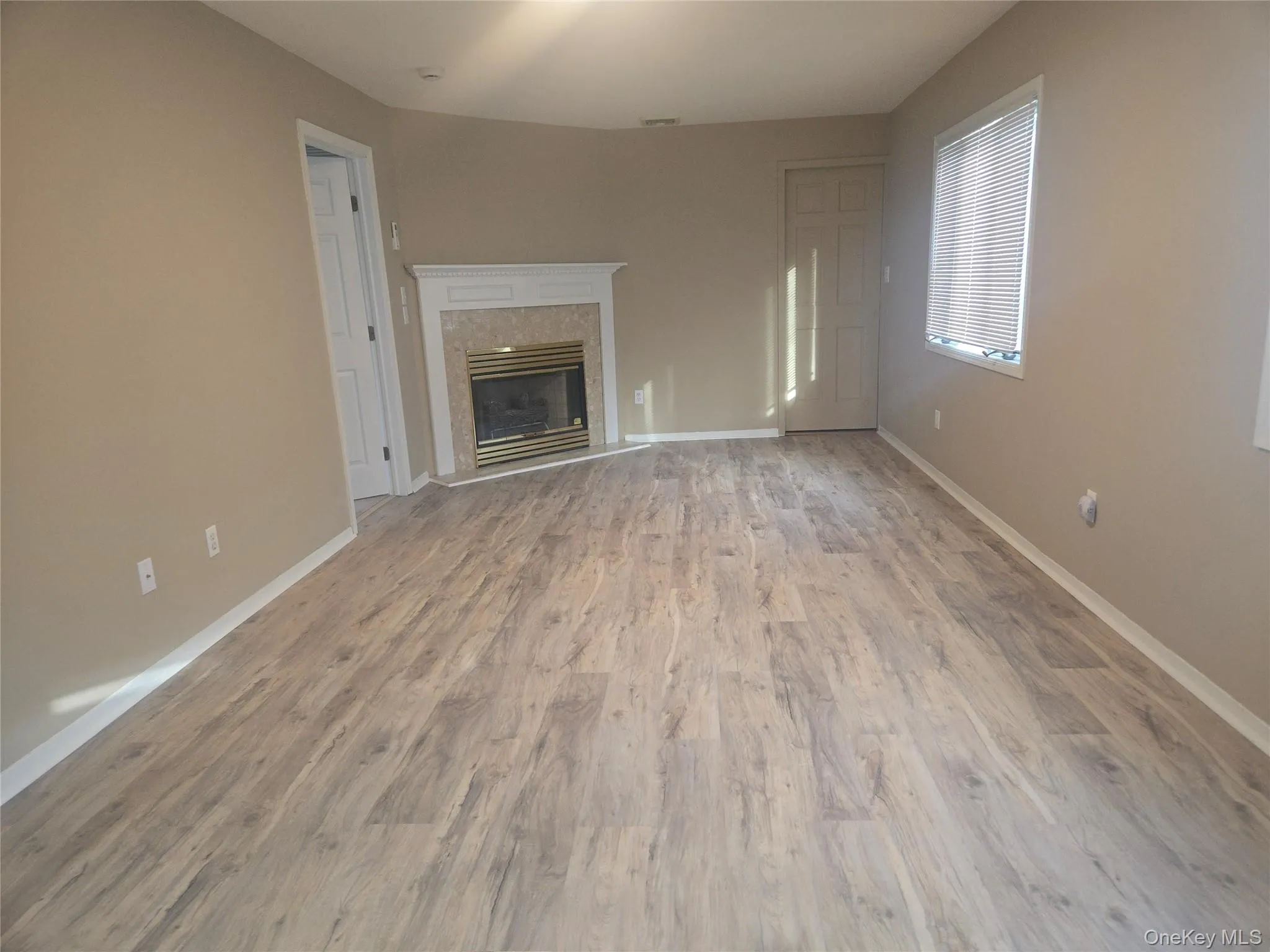 Unfurnished living room featuring a fireplace and light wood finished floors Unfurnished living room featuring a fireplace and light wood finished floors